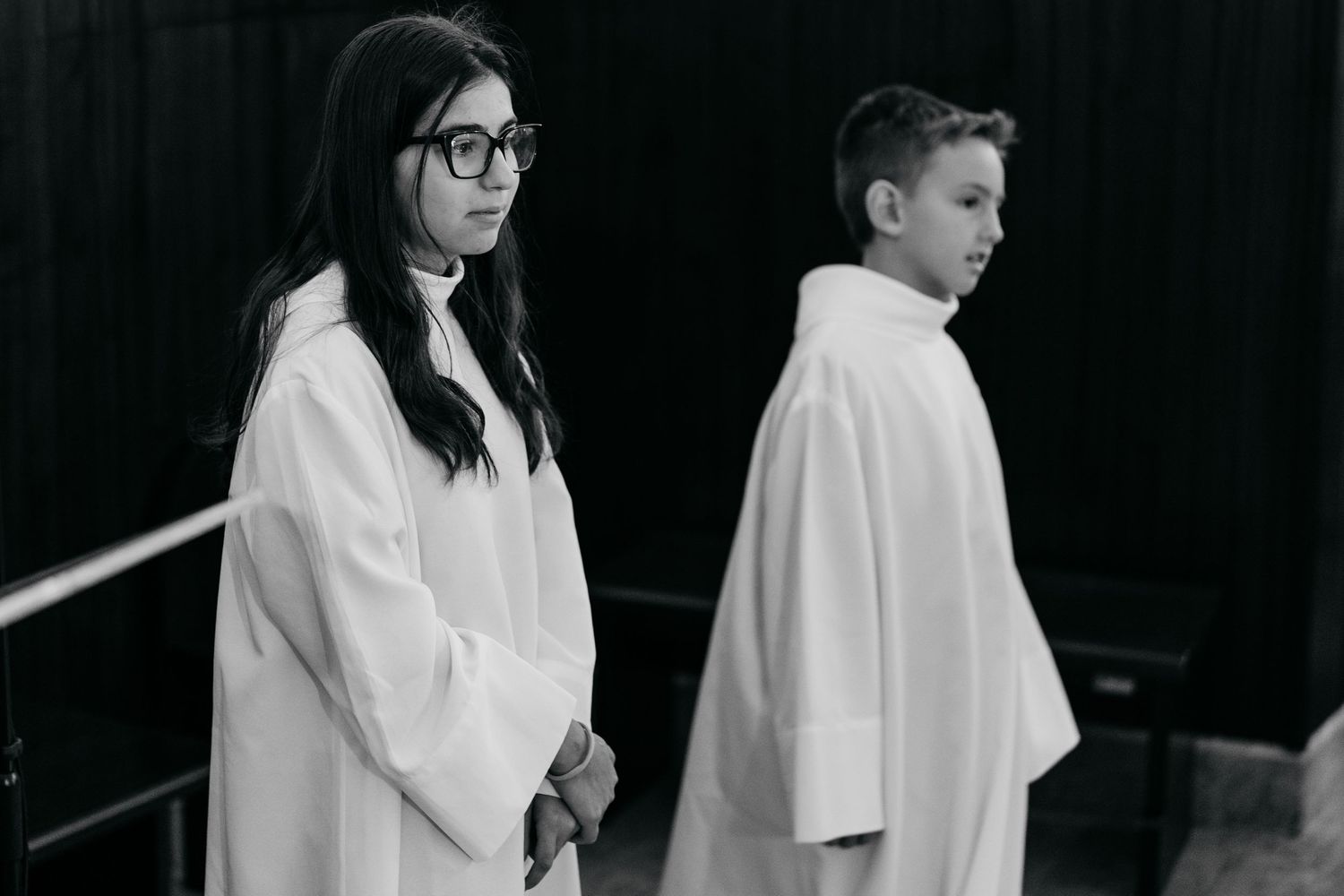 Two young altar servers in white robes stand solemnly in black and white church photo.