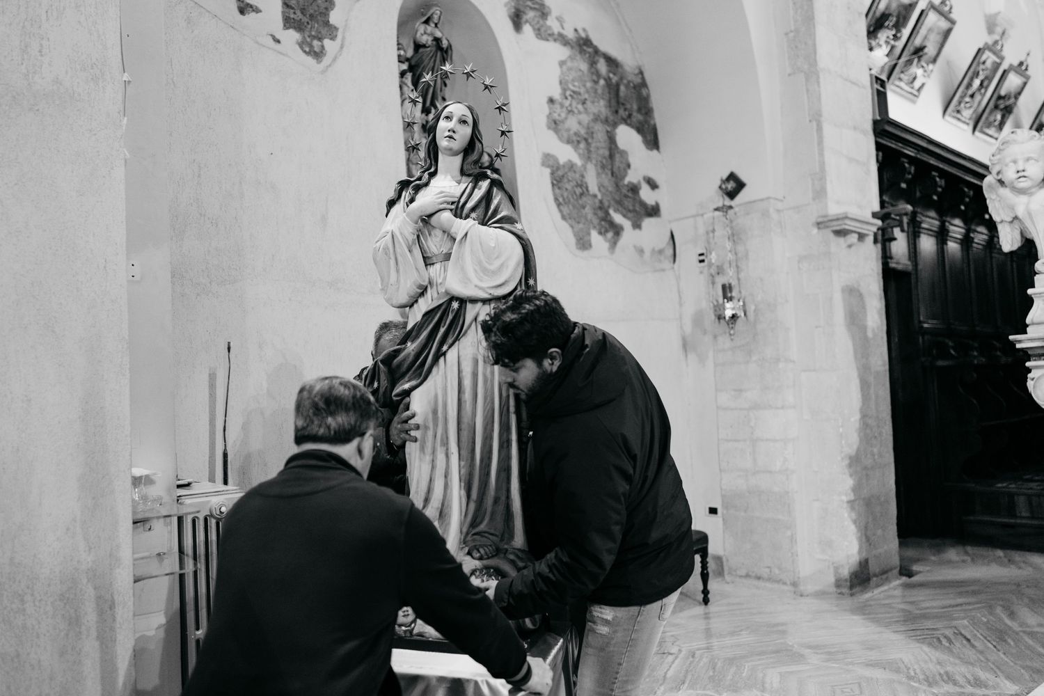 Two men kneeling before a religious statue inside a historic church in black and white photo.