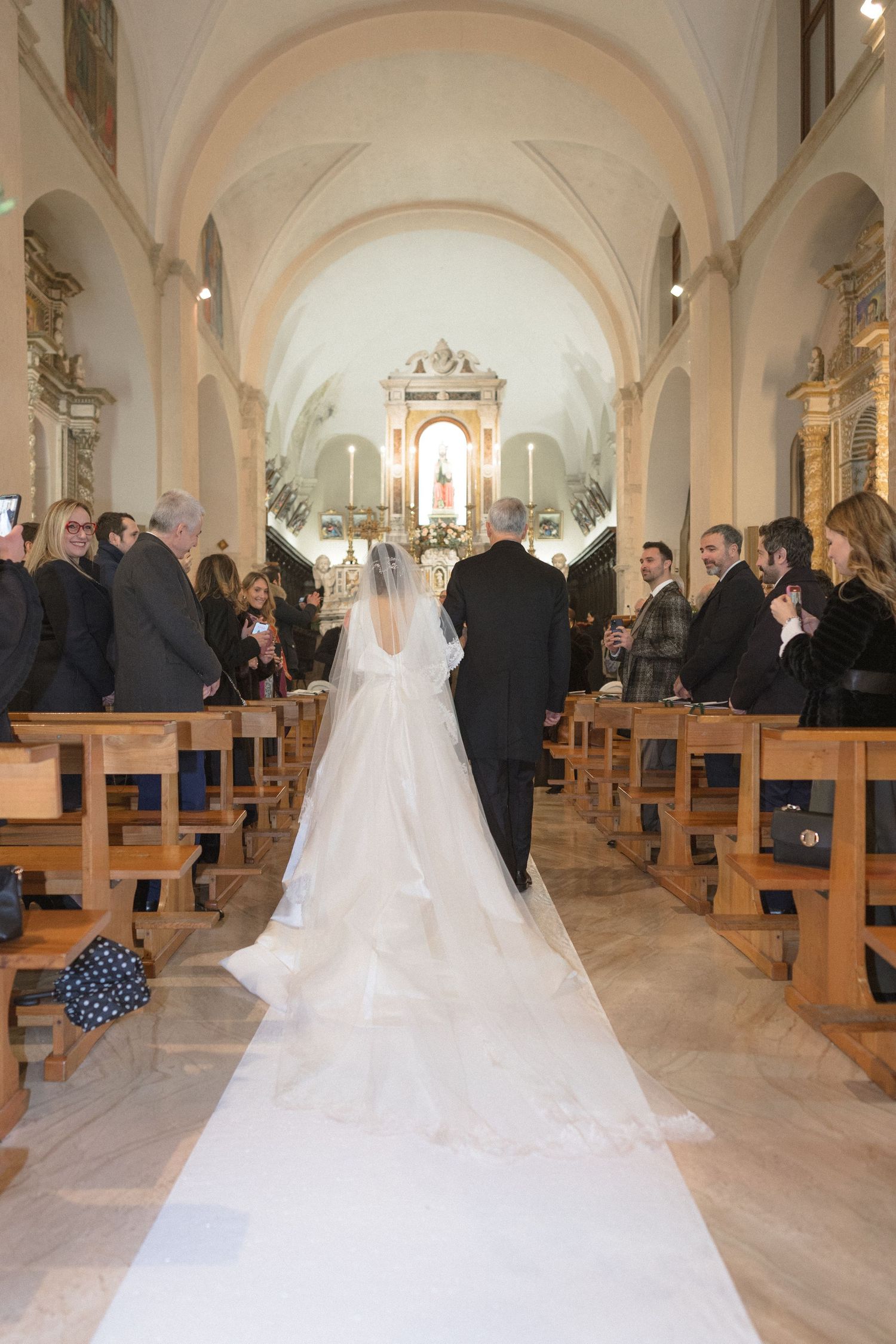 Bride walking down the aisle in a church wedding ceremony wearing a long white veil and gown.