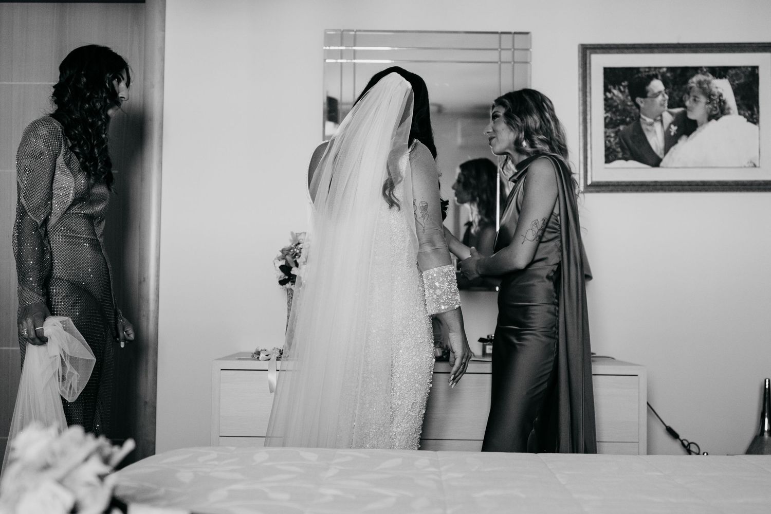 Black and white photo of wedding preparations showing bride in veil with attendants helping.