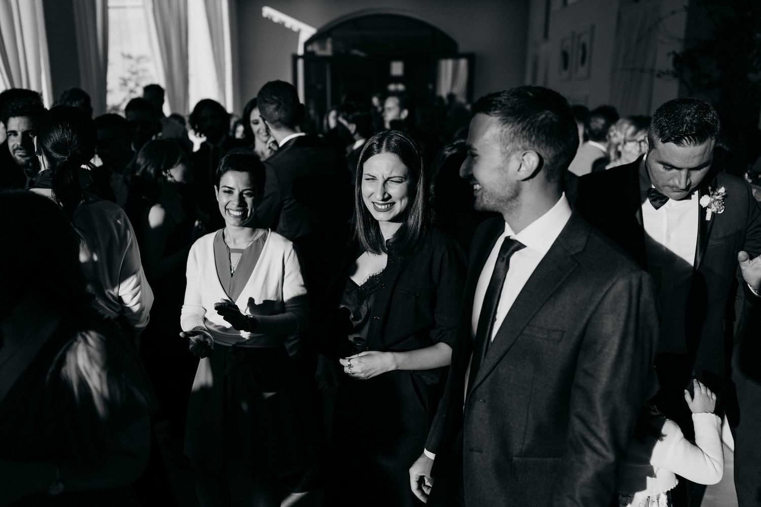 Guests in formal attire laugh and mingle at a elegant black and white wedding reception.