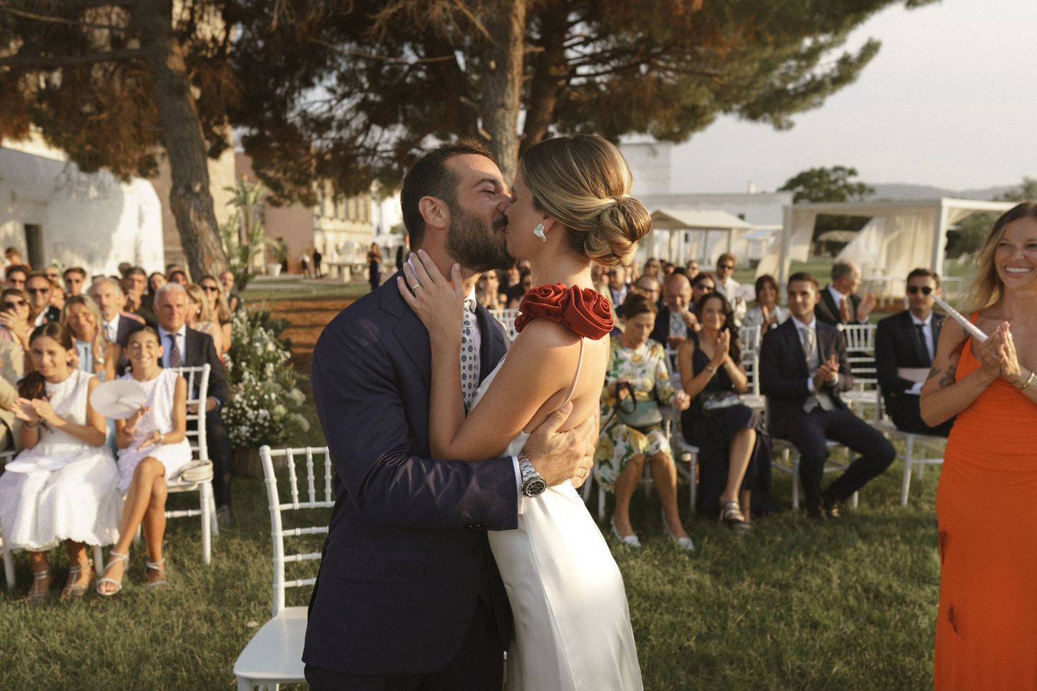 Newlyweds share their first kiss at an outdoor garden wedding while guests look on.