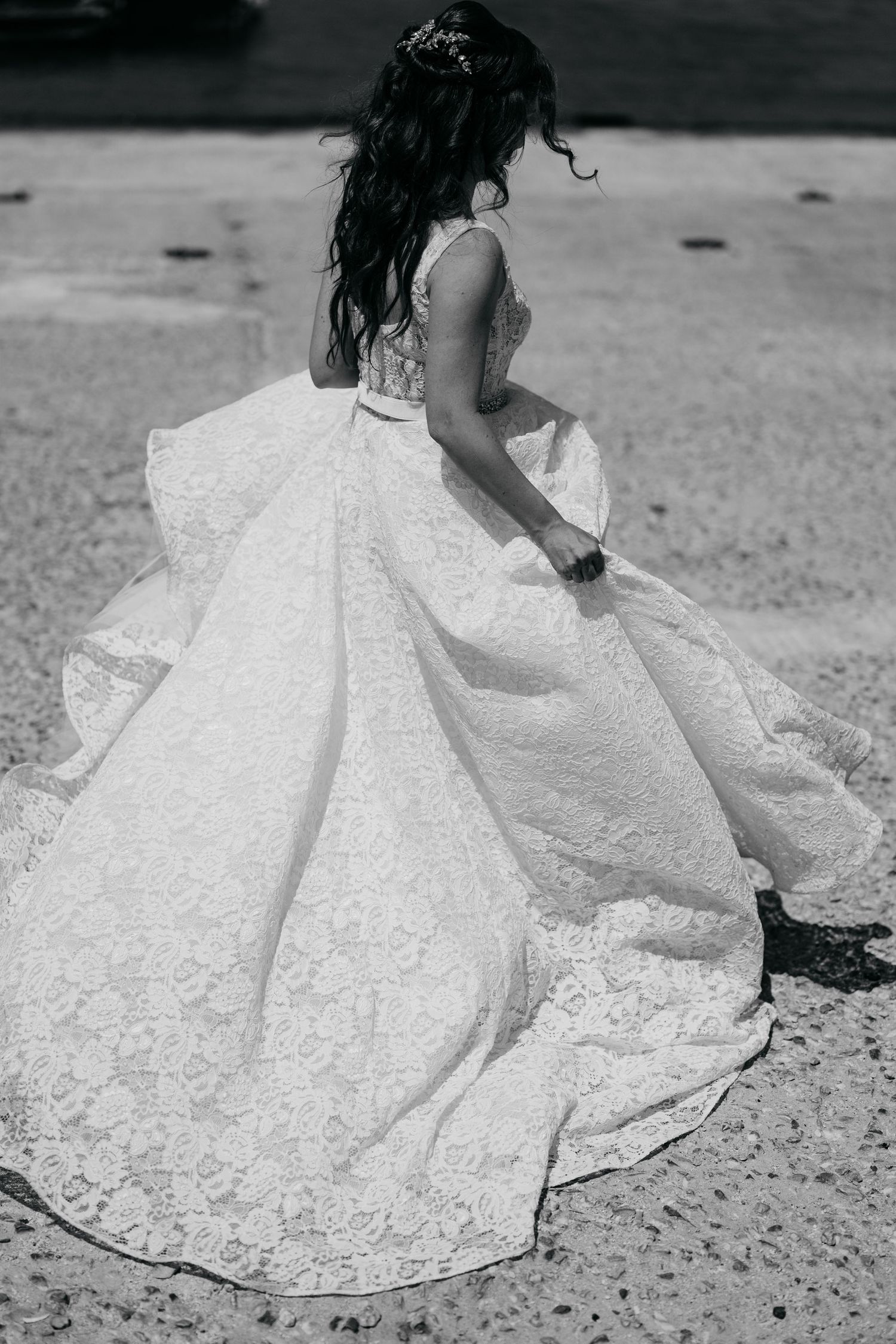 Black and white photo of a bride in an ornate lace ballgown with a flowing skirt spinning on a sandy beach.