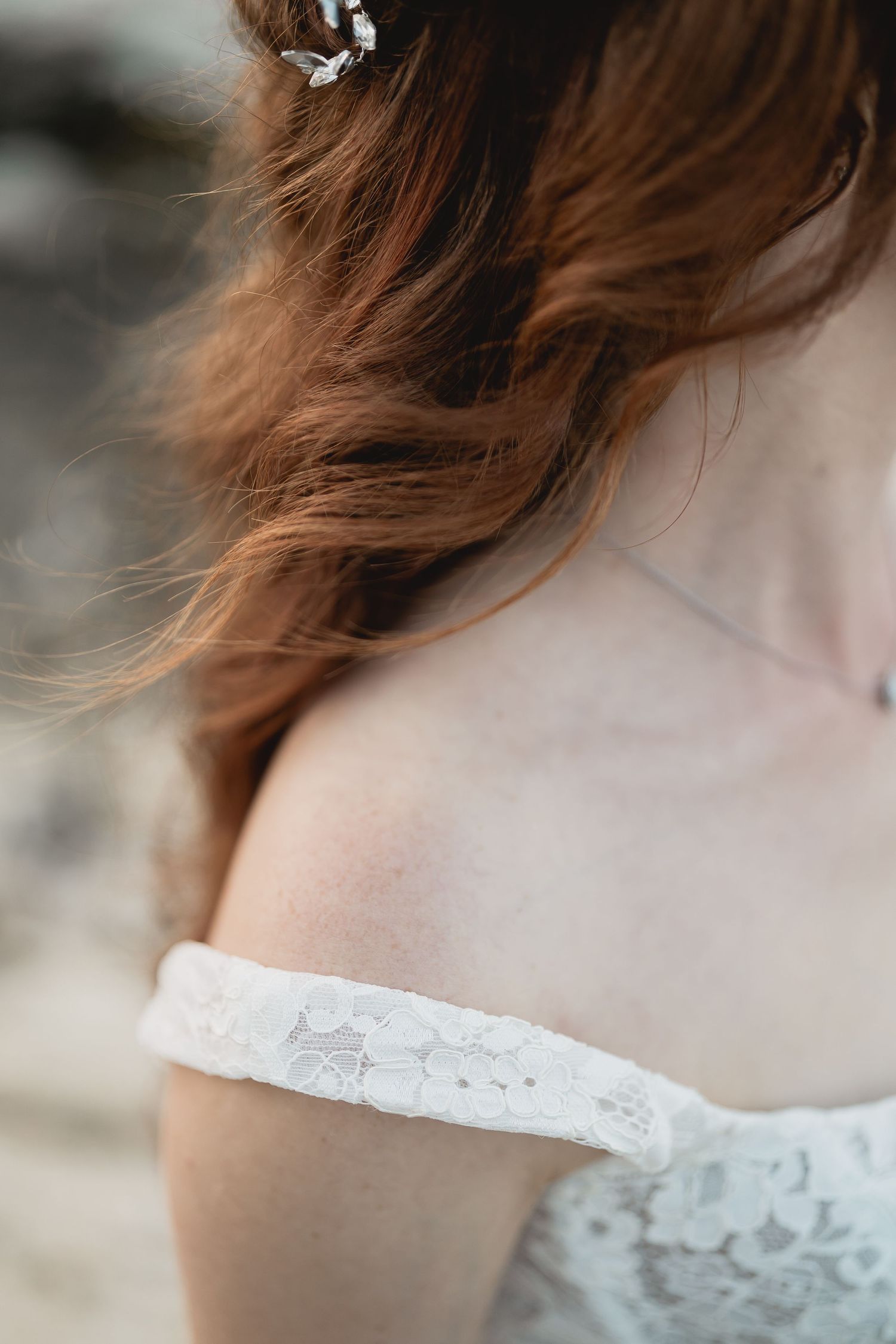Close-up detail of lace wedding dress sleeve and auburn hair.