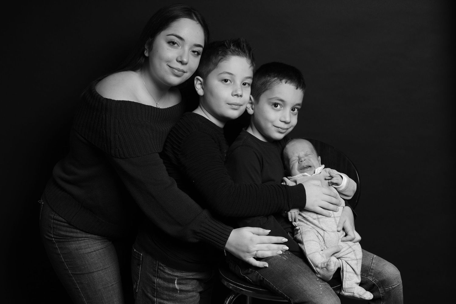 Black and white studio portrait of family members in matching black tops with an infant in white.