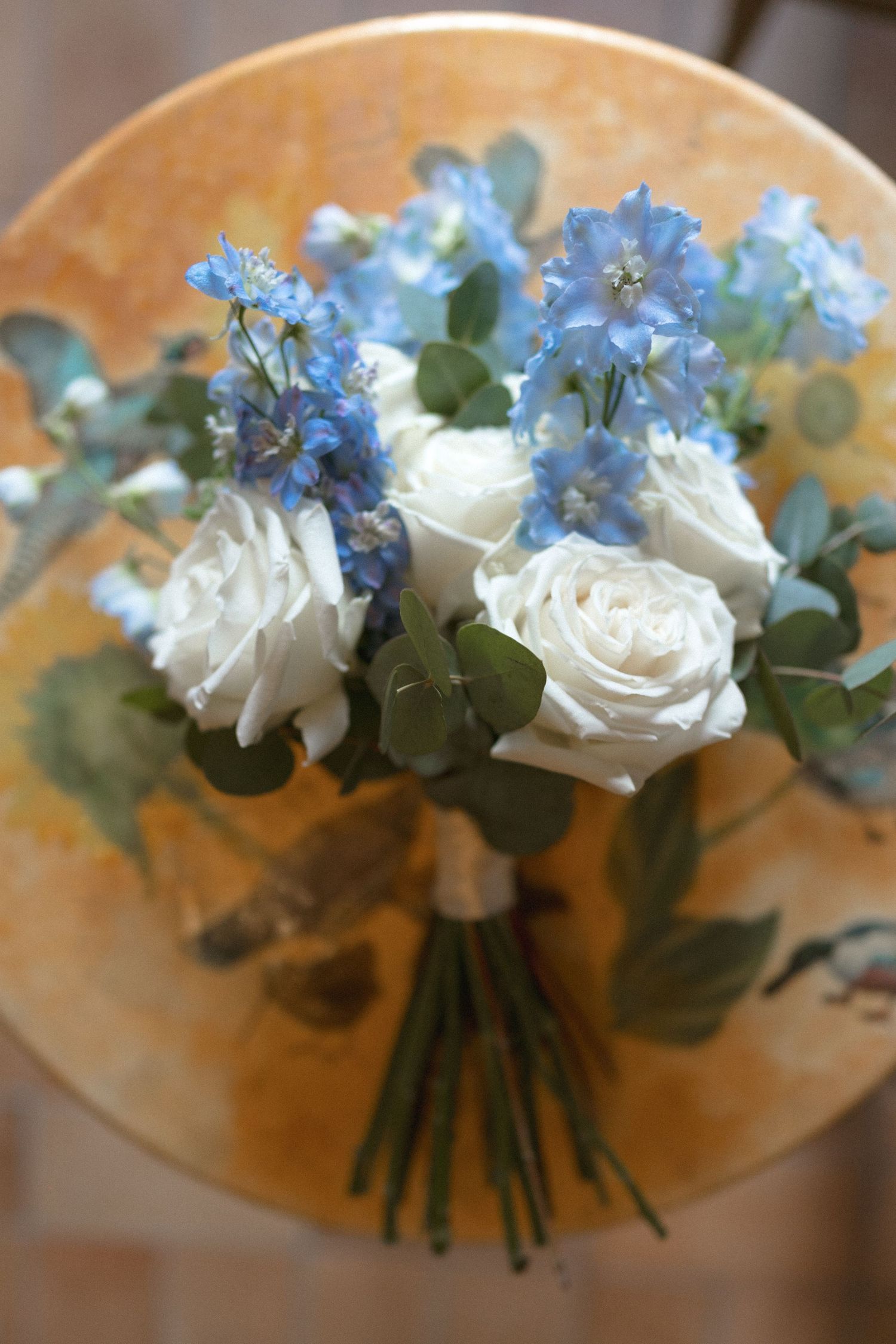 A delicate bouquet of white roses and blue forget-me-nots arranged with eucalyptus leaves on a wooden surface.