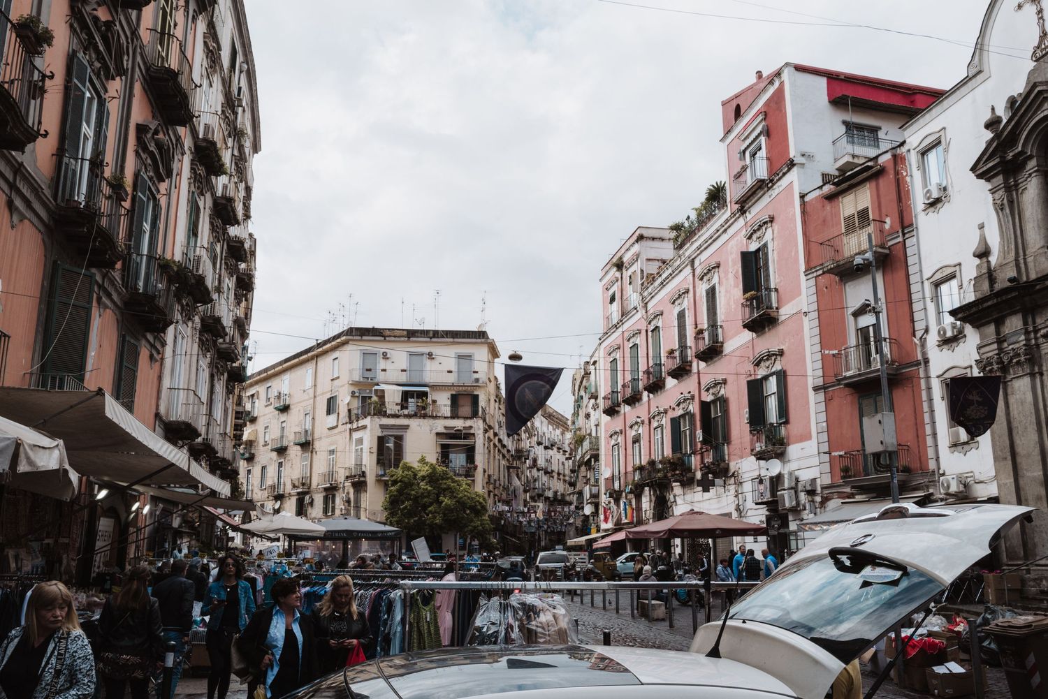 Busy street corner in an Italian neighborhood with pink buildings and parked cars.