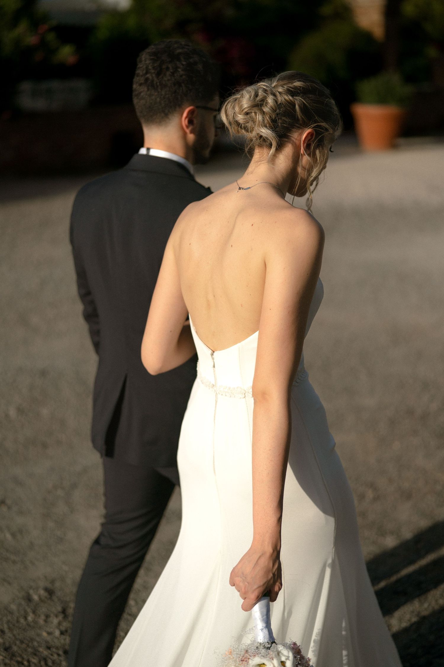 Back view of a white wedding dress with zipper detail against sunlit outdoor setting.