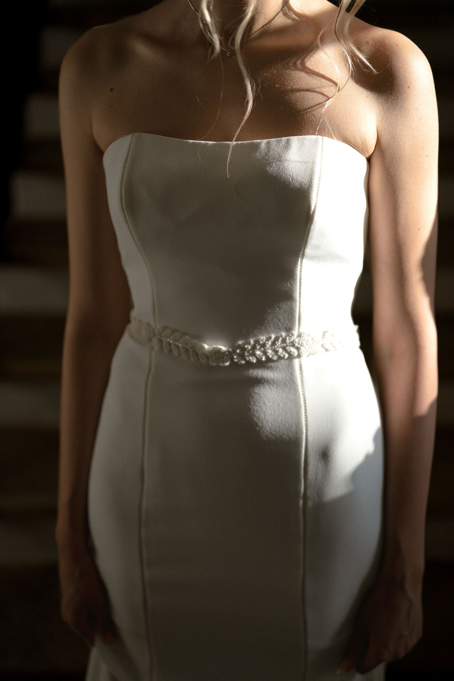 Close-up details of a white strapless wedding dress bodice with delicate beaded embellishments at the waist.