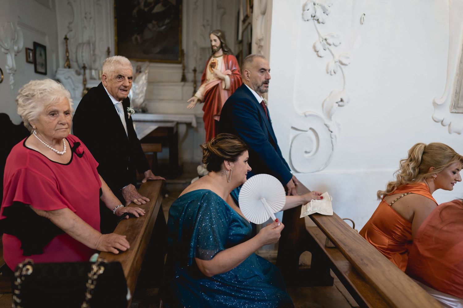Wedding guests seated in wooden pews during a church ceremony with decorative white walls.