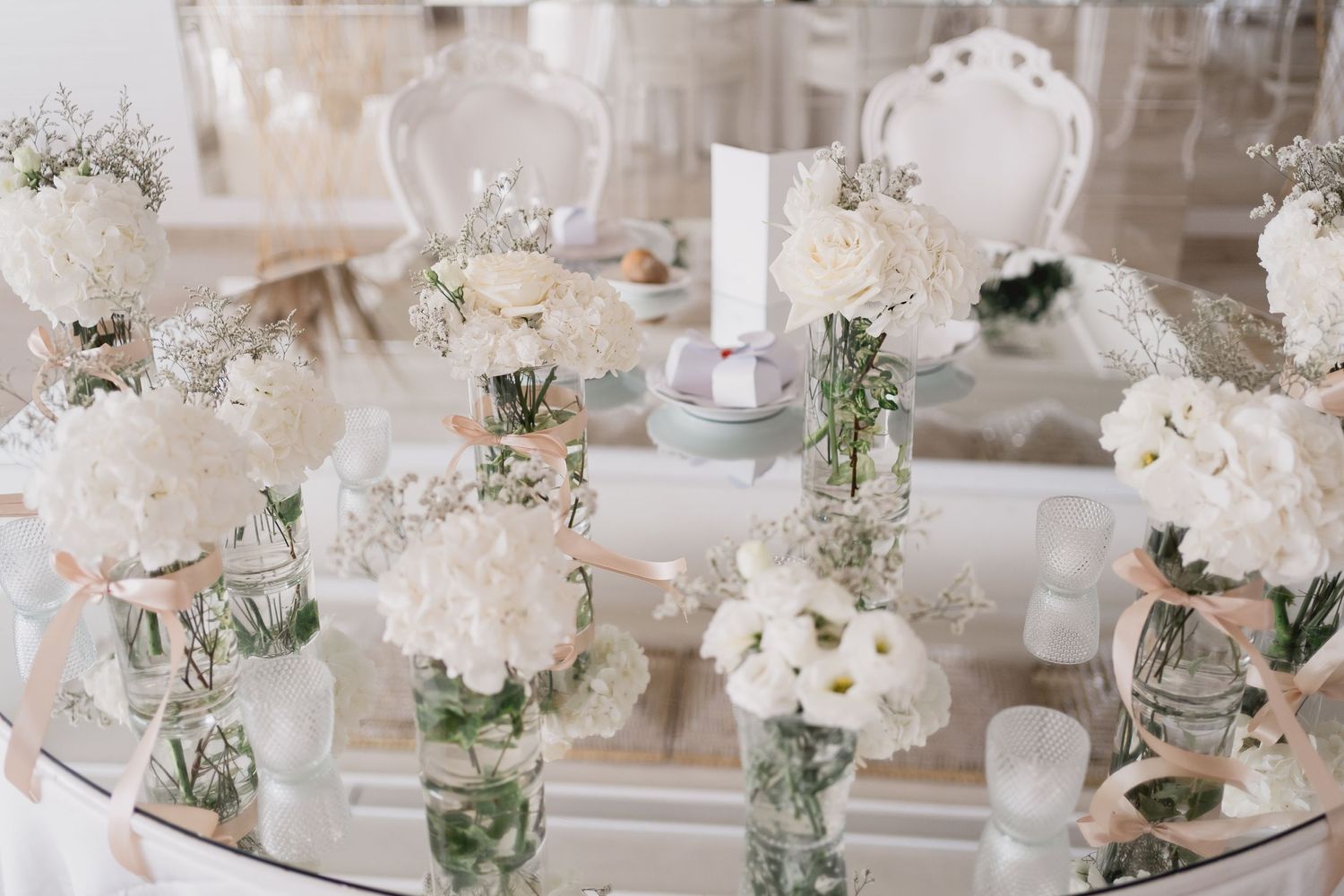 Elegant white floral wedding reception centerpieces arranged on mirrored table.