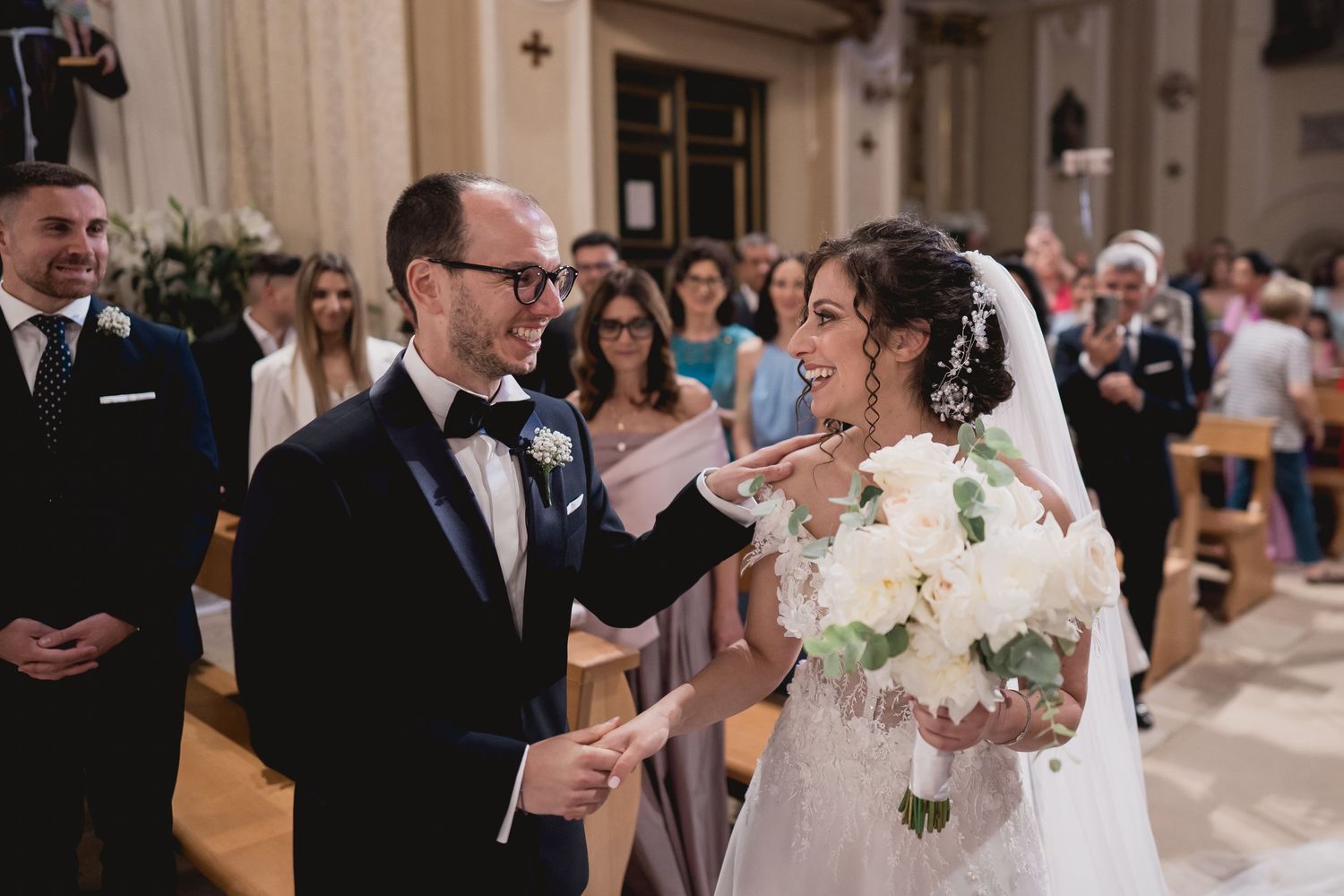 Interior church wedding ceremony with floral bouquet and gathered guests.