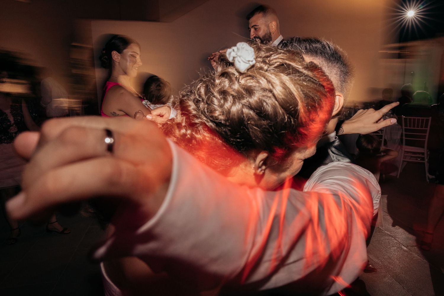 Motion-blurred photograph captures dancing movements at a lively party with red lighting effects.