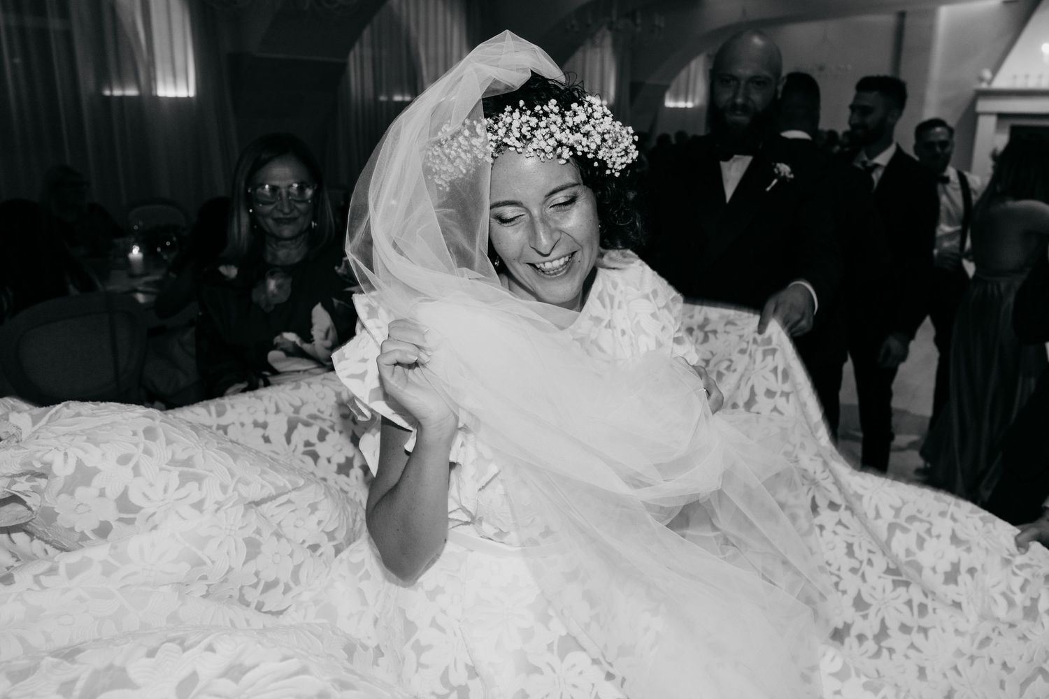A bride in a voluminous lace wedding gown and veil smiles during her wedding celebration.