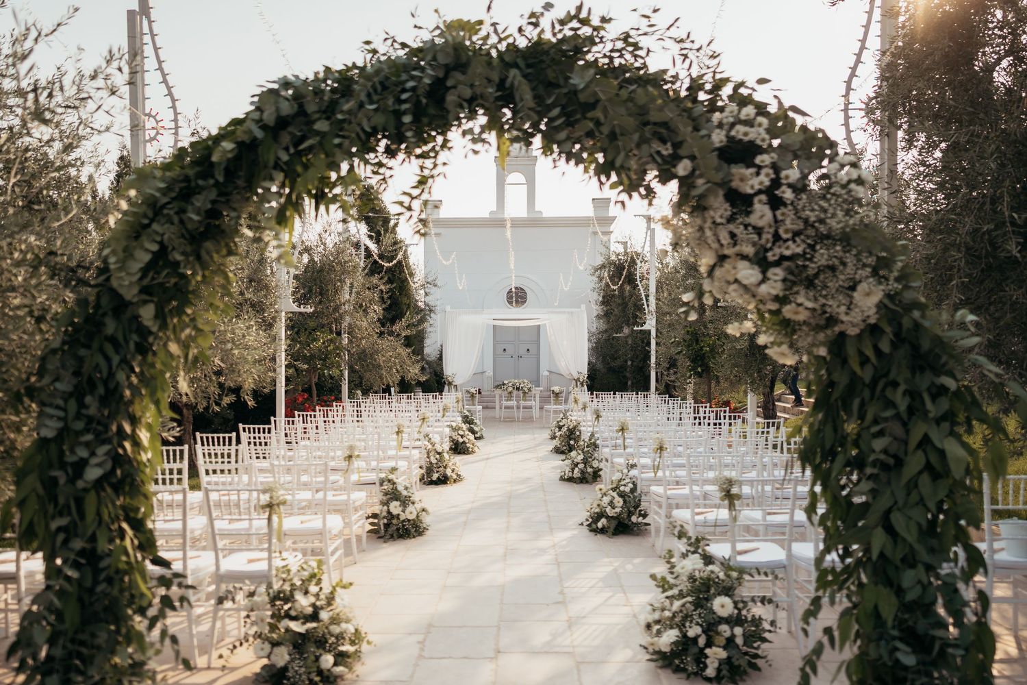 Beautiful floral arch over white chairs set up for an outdoor wedding ceremony.