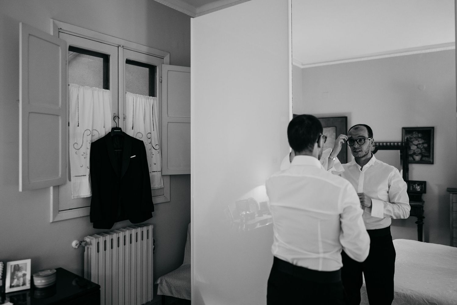 Wedding preparation room with formal attire hanging by windows in black and white.