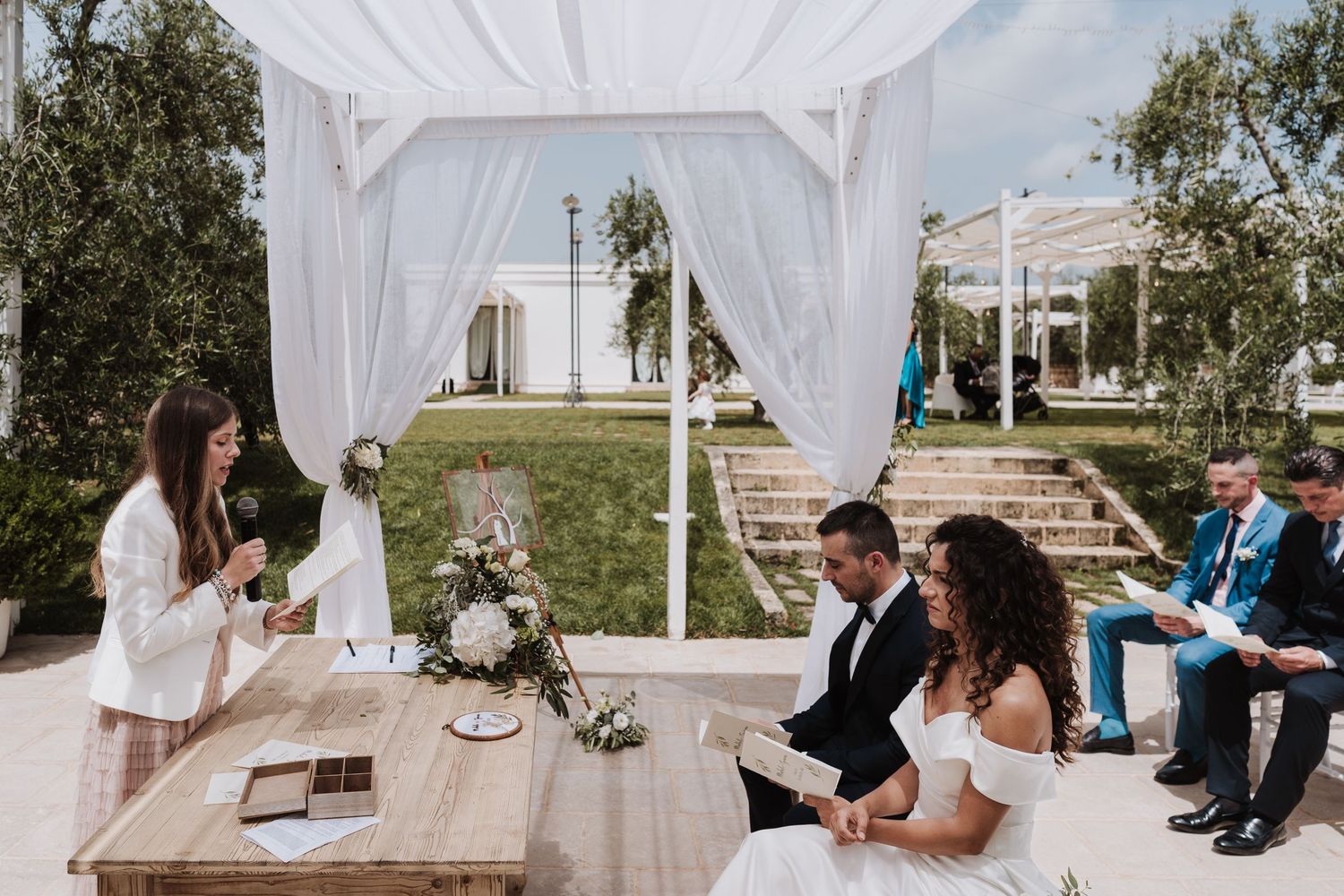 Outdoor wedding ceremony under white draped gazebo with wooden table and floral centerpiece.