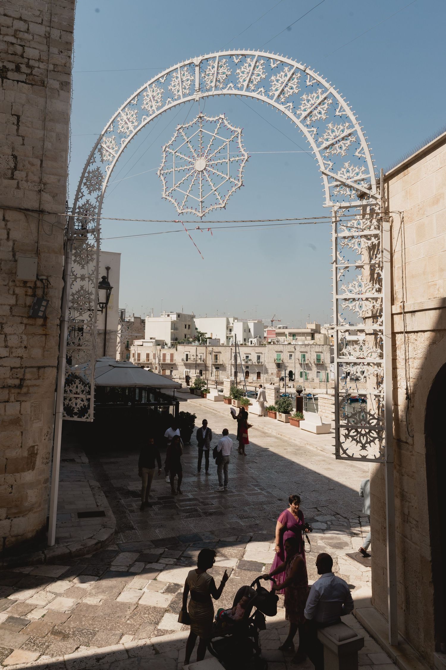 Decorative white arch frames a city street with people walking beneath it.