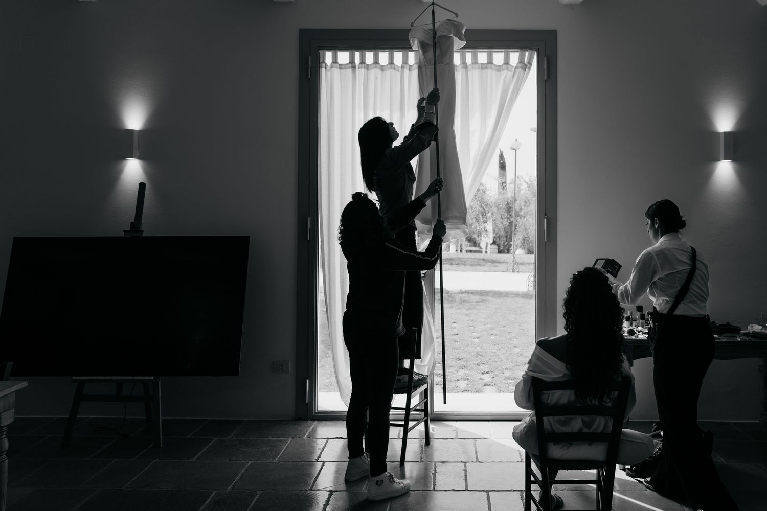 Black and white image of silhouettes preparing in a room with natural window light.