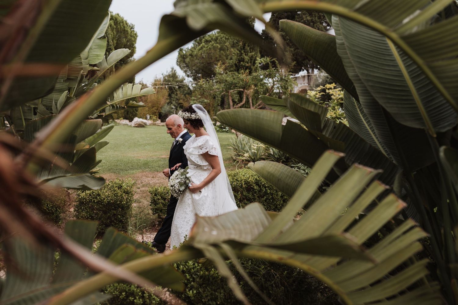 Wedding couple embracing among tropical palm leaves in garden setting.