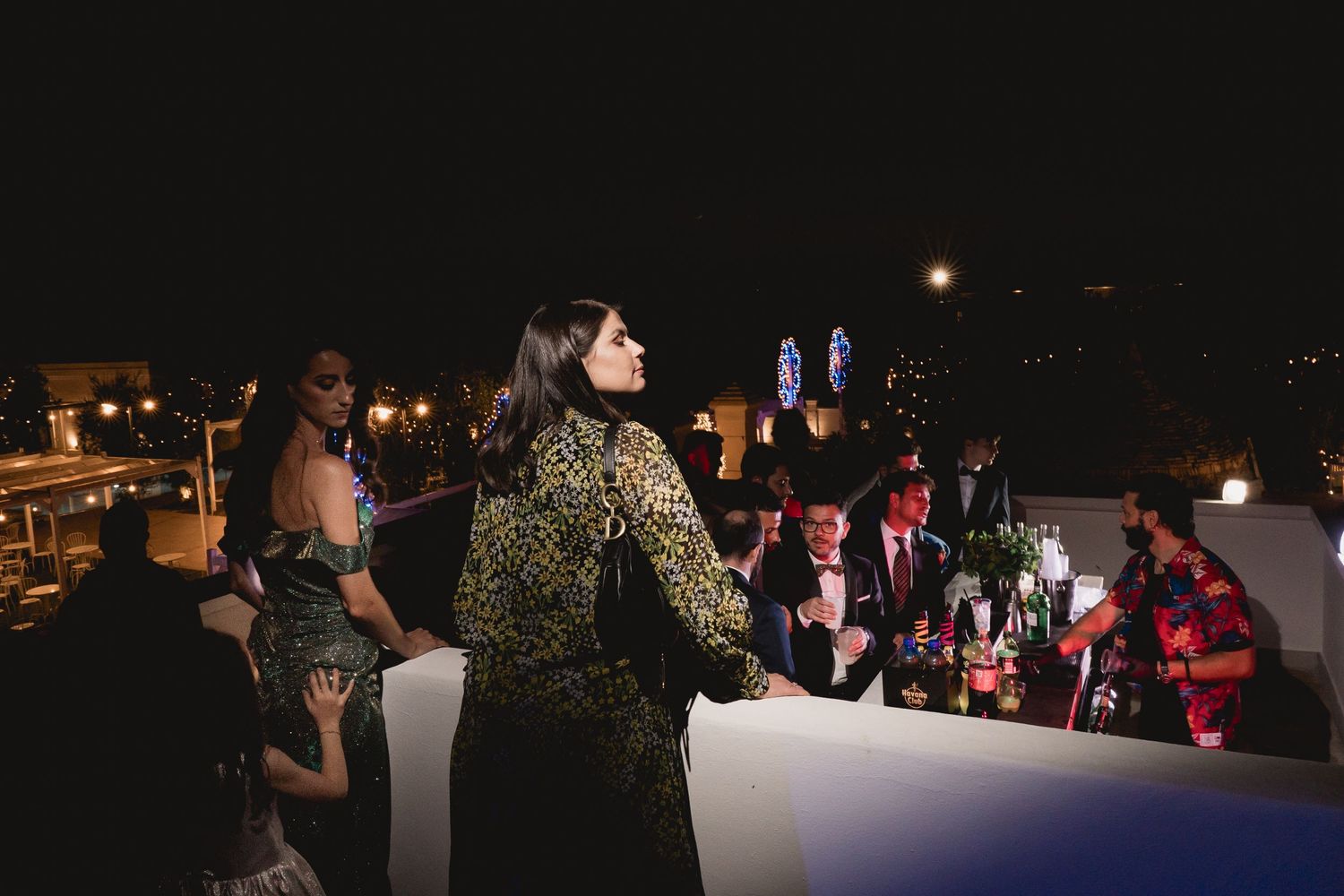 Evening rooftop party scene with city lights in background.