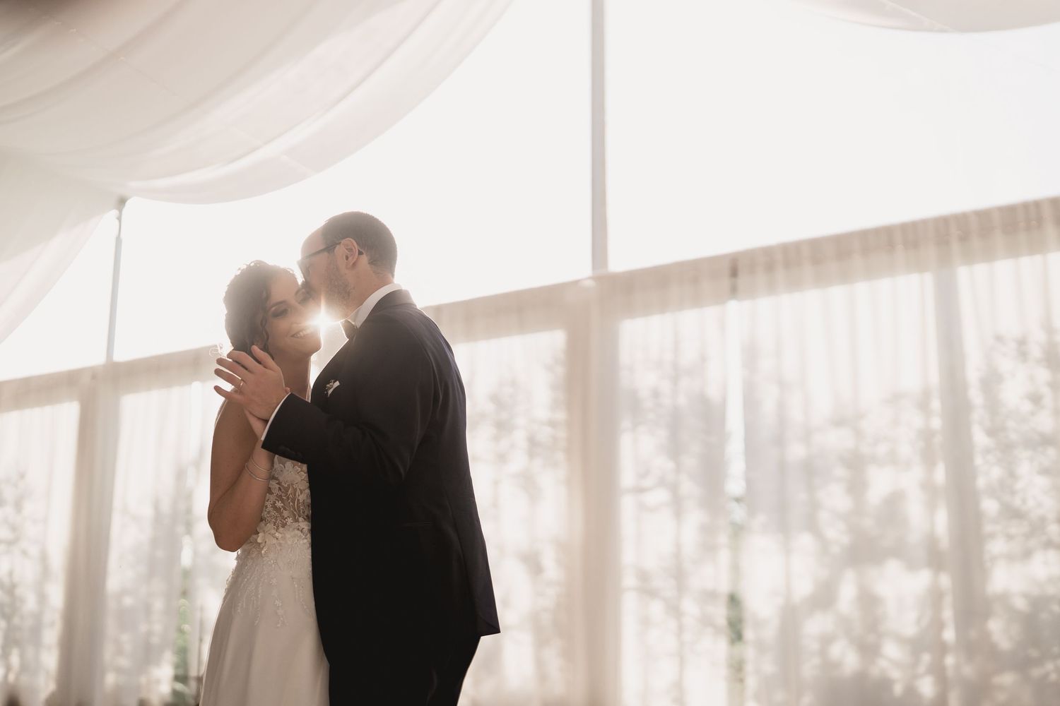 A romantic silhouette of newlyweds sharing a tender moment by sunlit windows at their wedding ceremony.