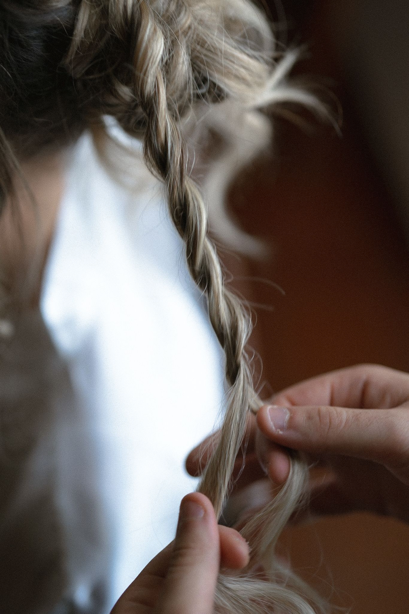Close-up shots showing hands braiding delicate strands of blonde hair in a detailed styling sequence.