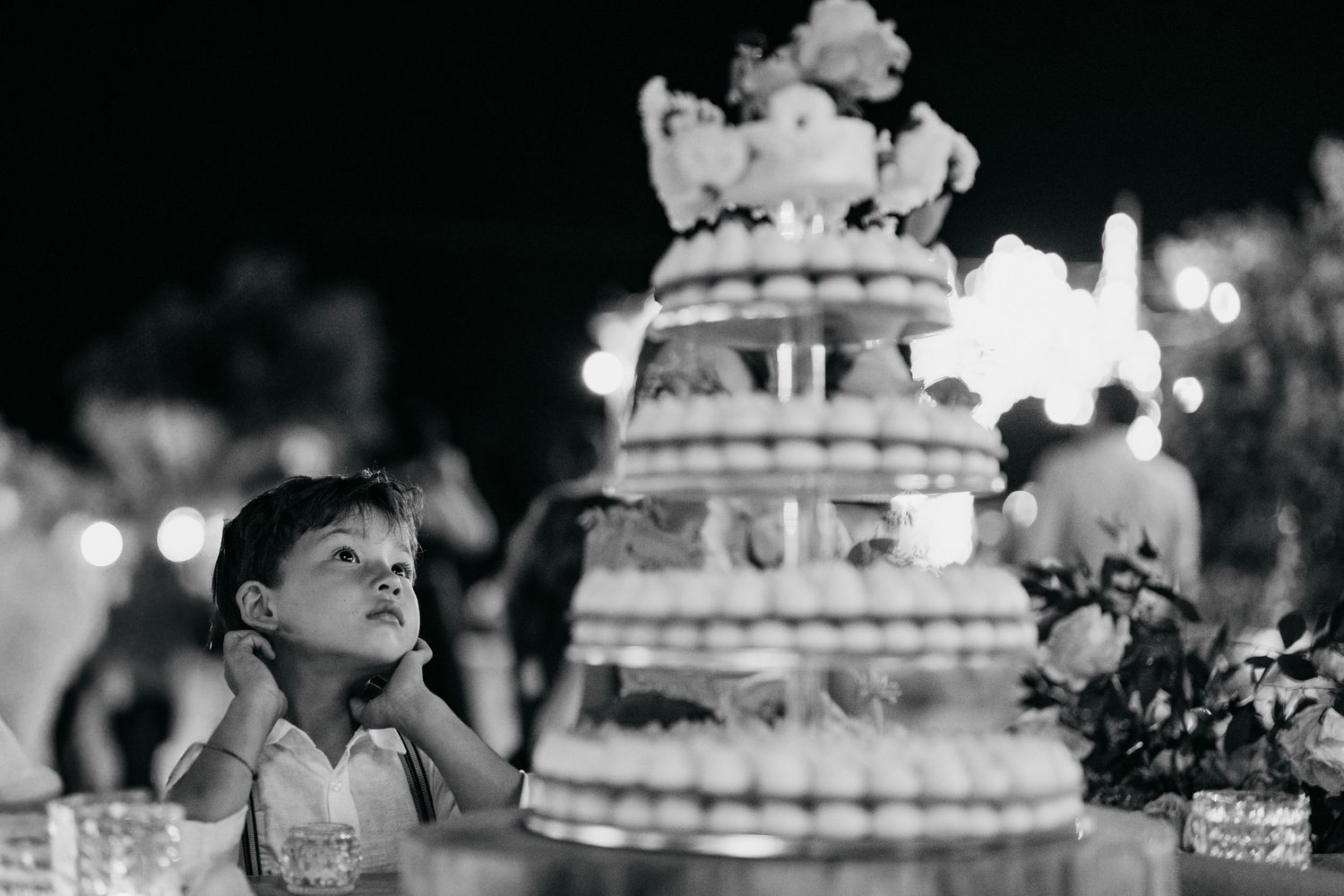 Young child gazes in wonder at an elegant tiered wedding cake illuminated by soft lighting.