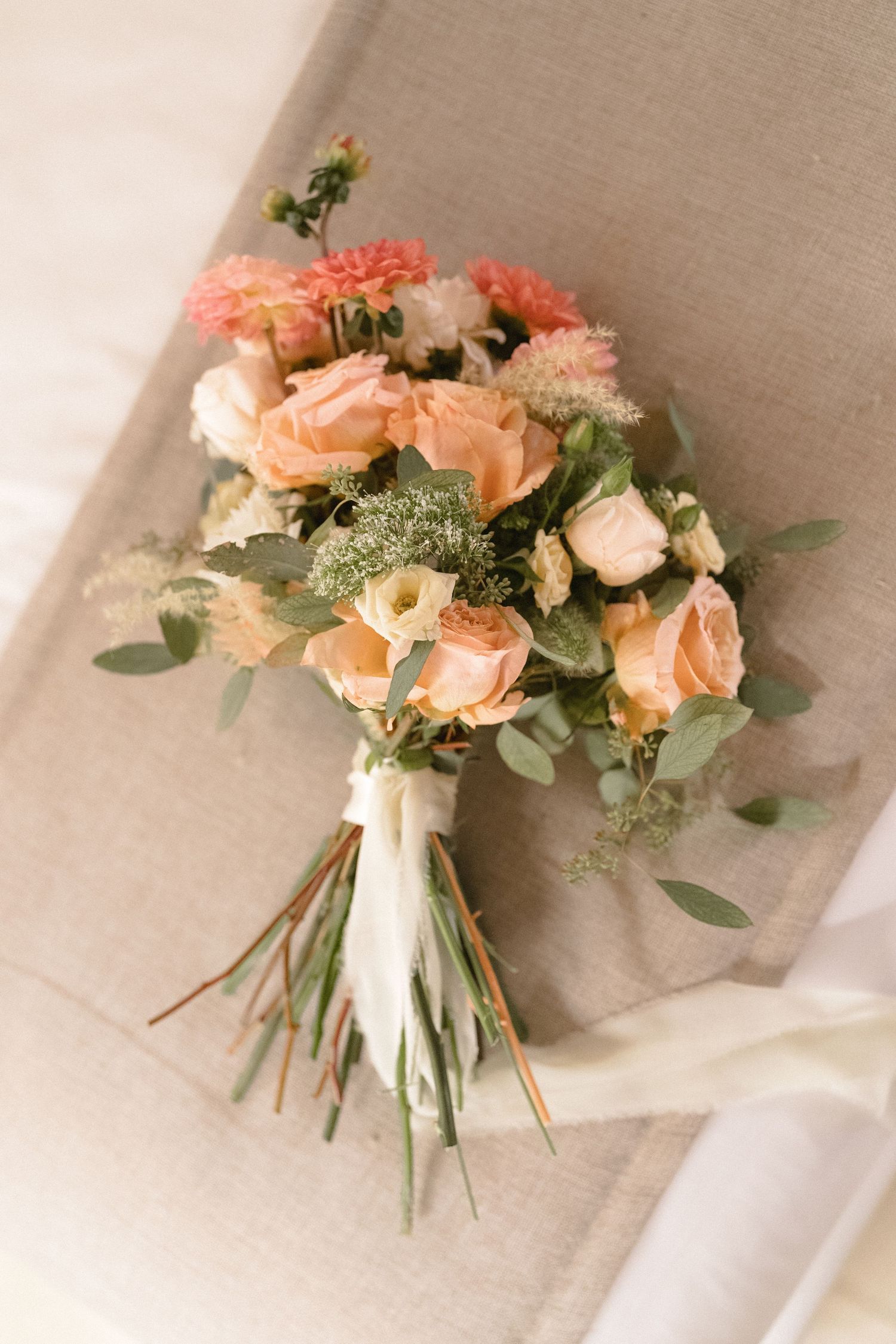 A romantic peach and coral wedding bouquet with roses and eucalyptus wrapped in white ribbon.