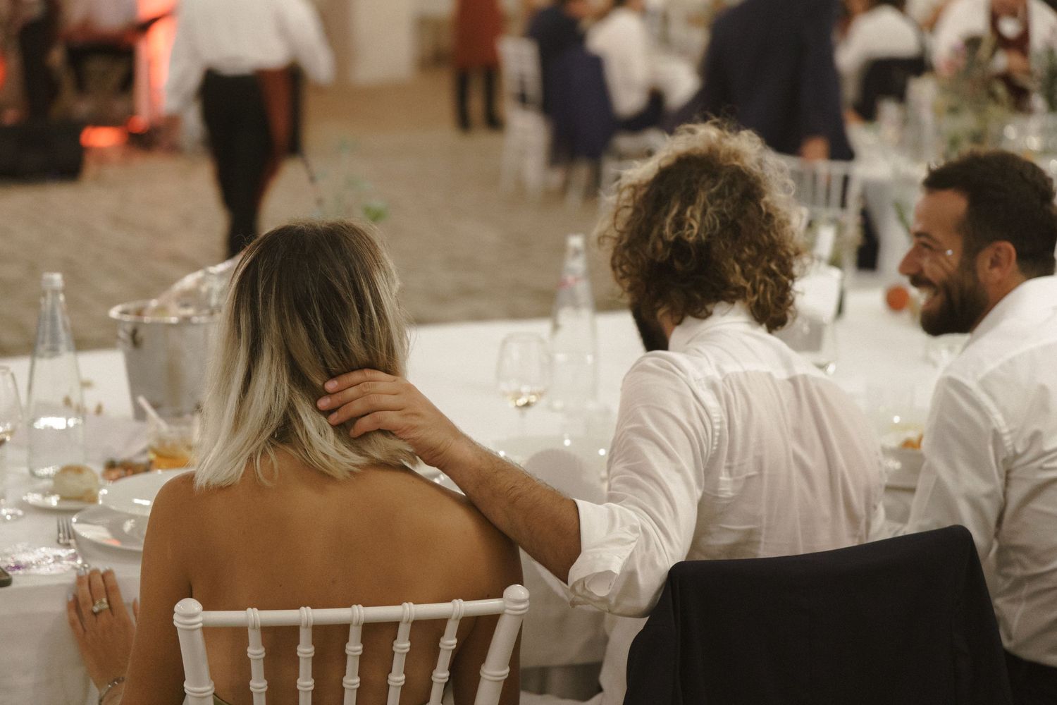 Guests seated at an elegant wedding reception dinner with white chairs and table settings.