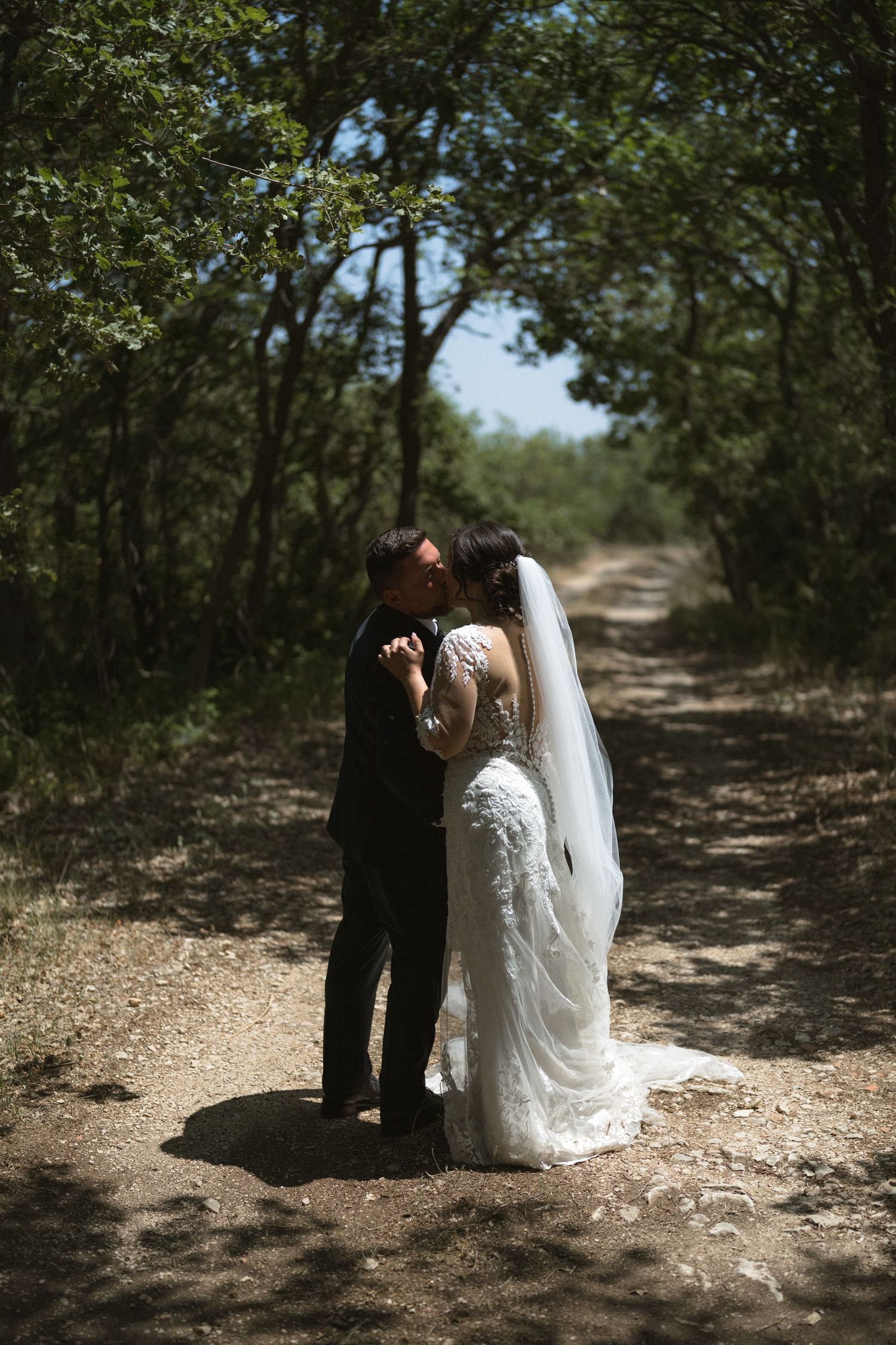 Couple sharing intimate moment on wooded path during wedding photoshoot.