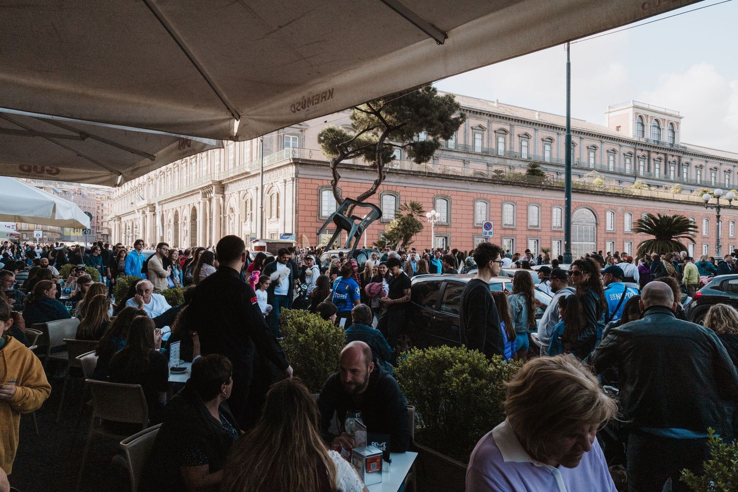 Large crowd gathers outside under canopies at an urban public event.