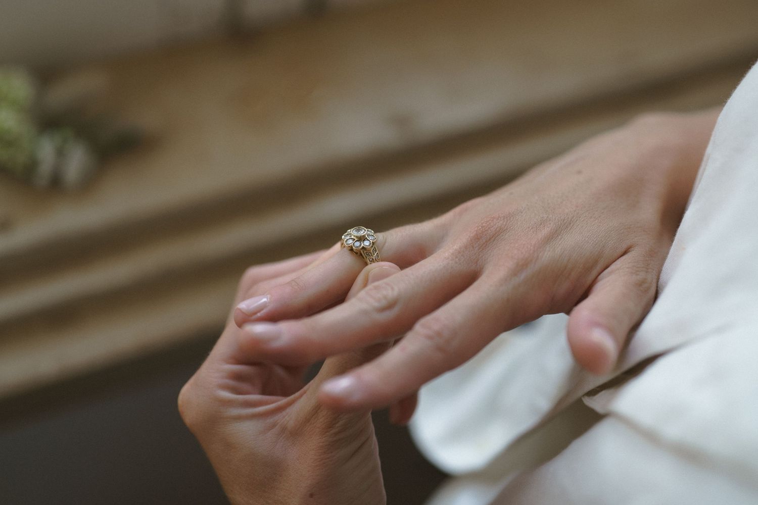 Close-up view of a diamond engagement ring on someones hand against a white fabric background.