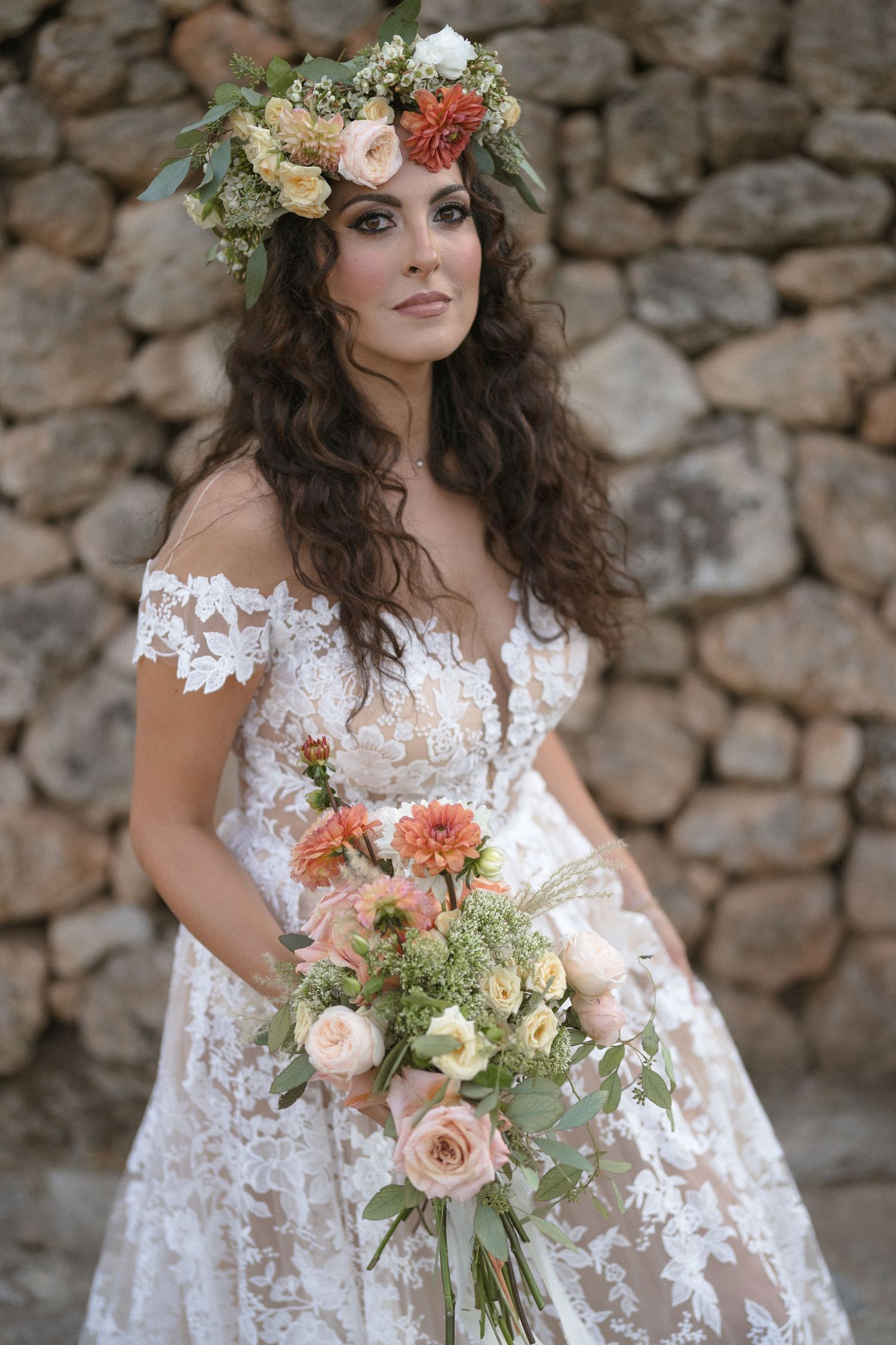 Bridal portrait with floral crown and lace dress against stone wall.