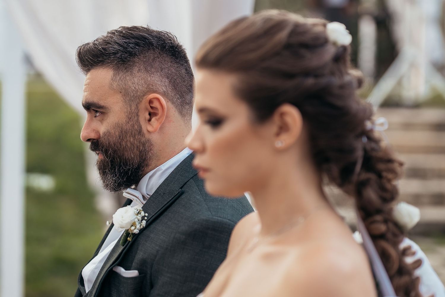 An elegant wedding couple in formal attire poses during their outdoor ceremony.