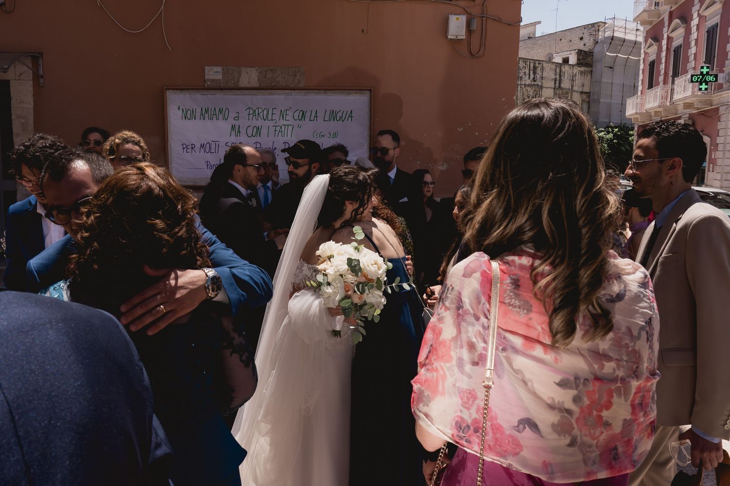 Wedding guests gather outside in celebration with the bride holding a white bouquet.
