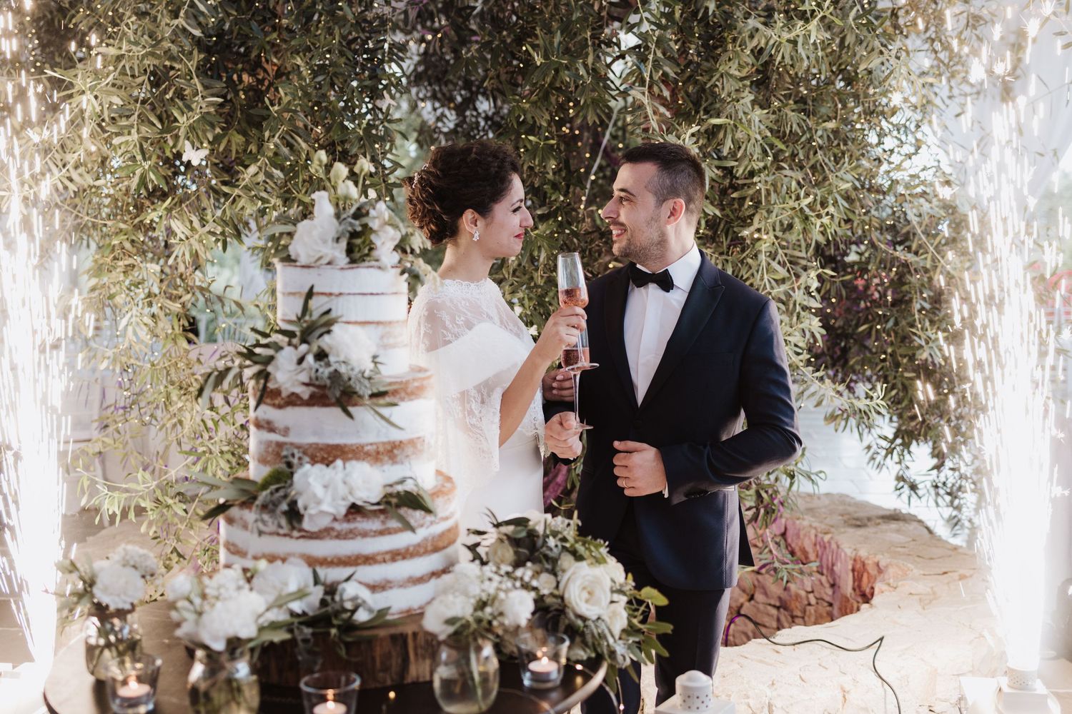 Elegant wedding display featuring a multi-tiered cake surrounded by lush greenery and soft lighting.