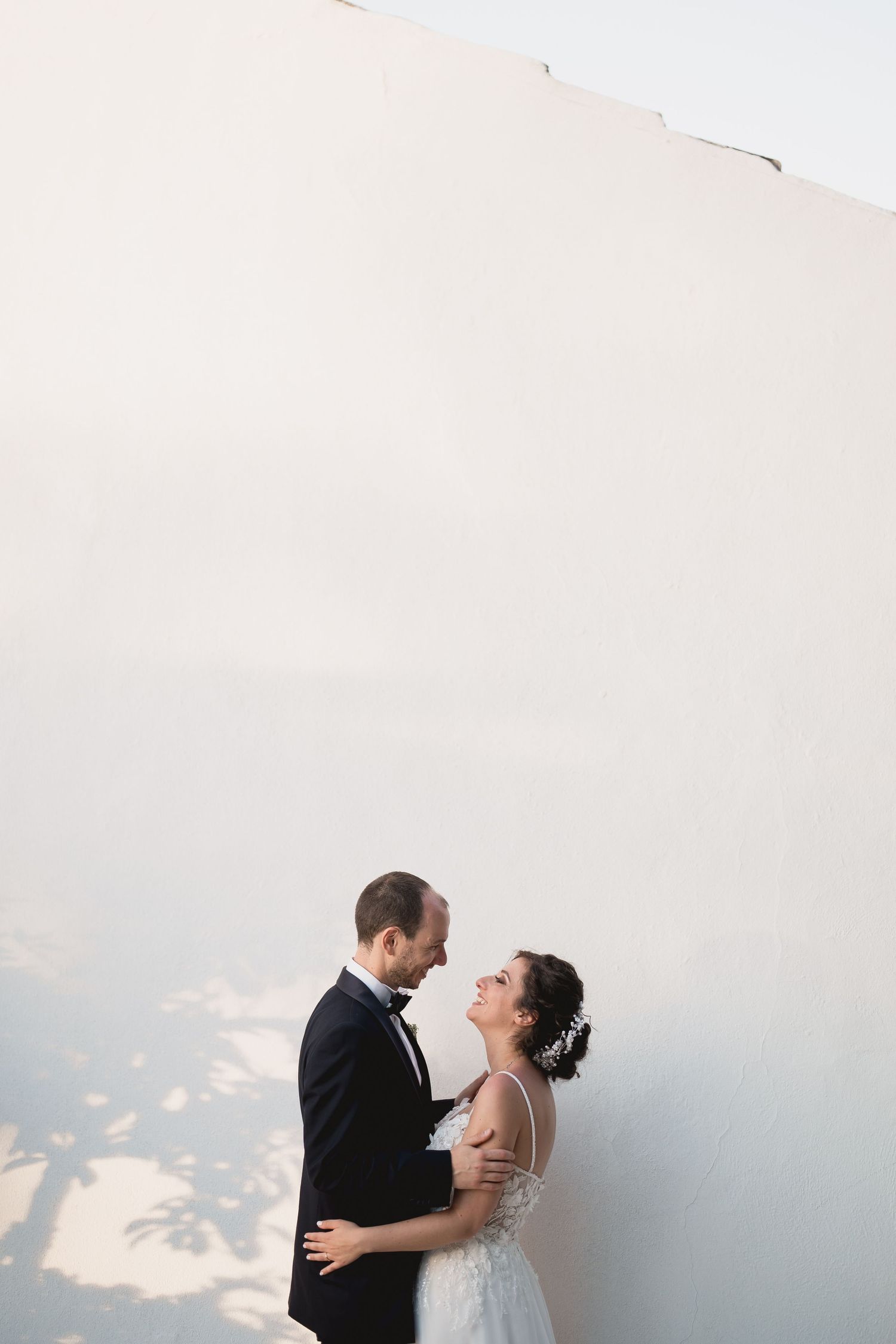 A tender wedding portrait against a minimalist white wall with beautiful afternoon light and shadows.
