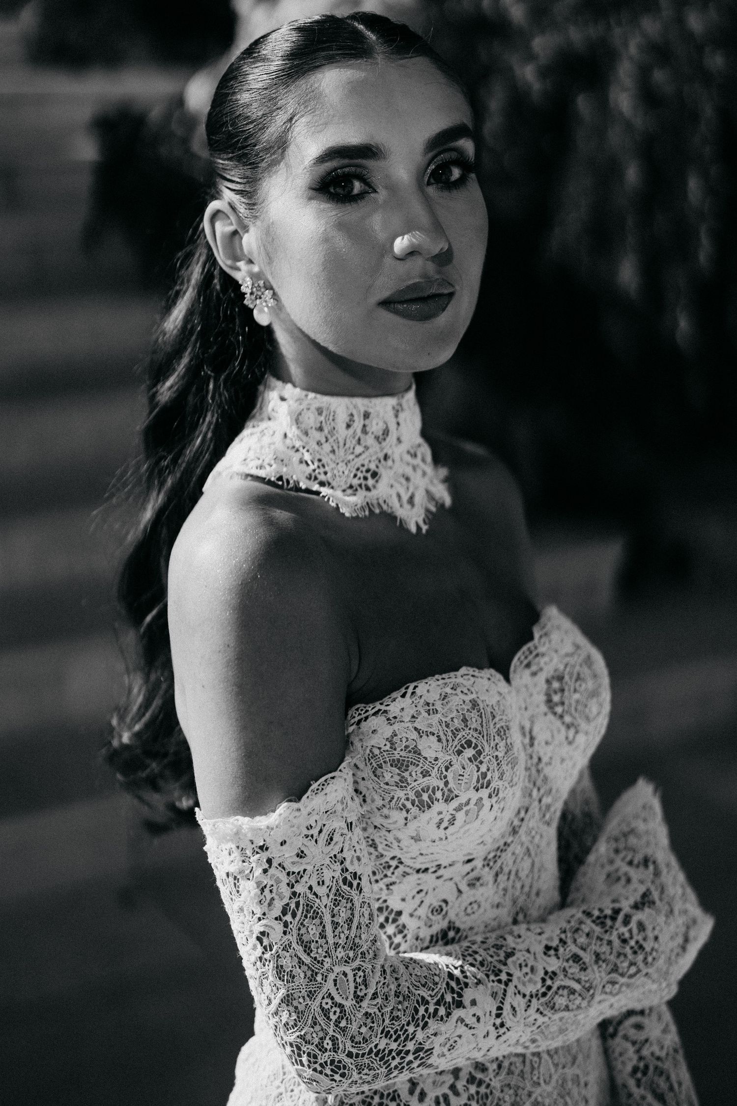 Black and white portrait of a bride with a sleek ponytail wearing an off-shoulder lace wedding gown with a high lace collar.