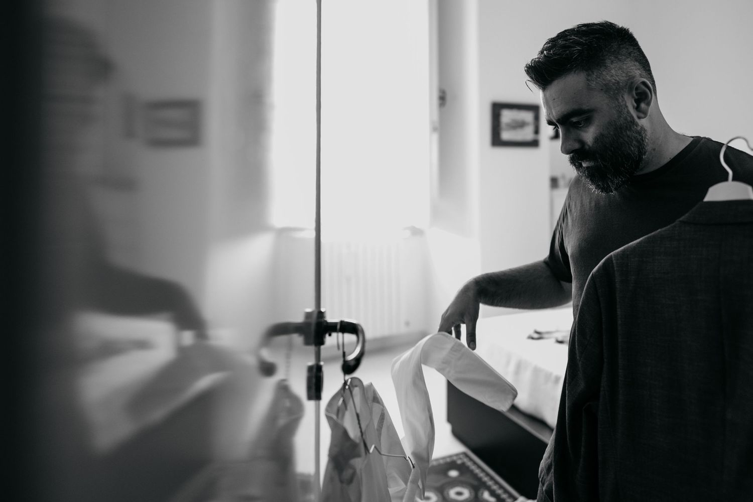 Person in dark clothing getting dressed in monochrome interior.