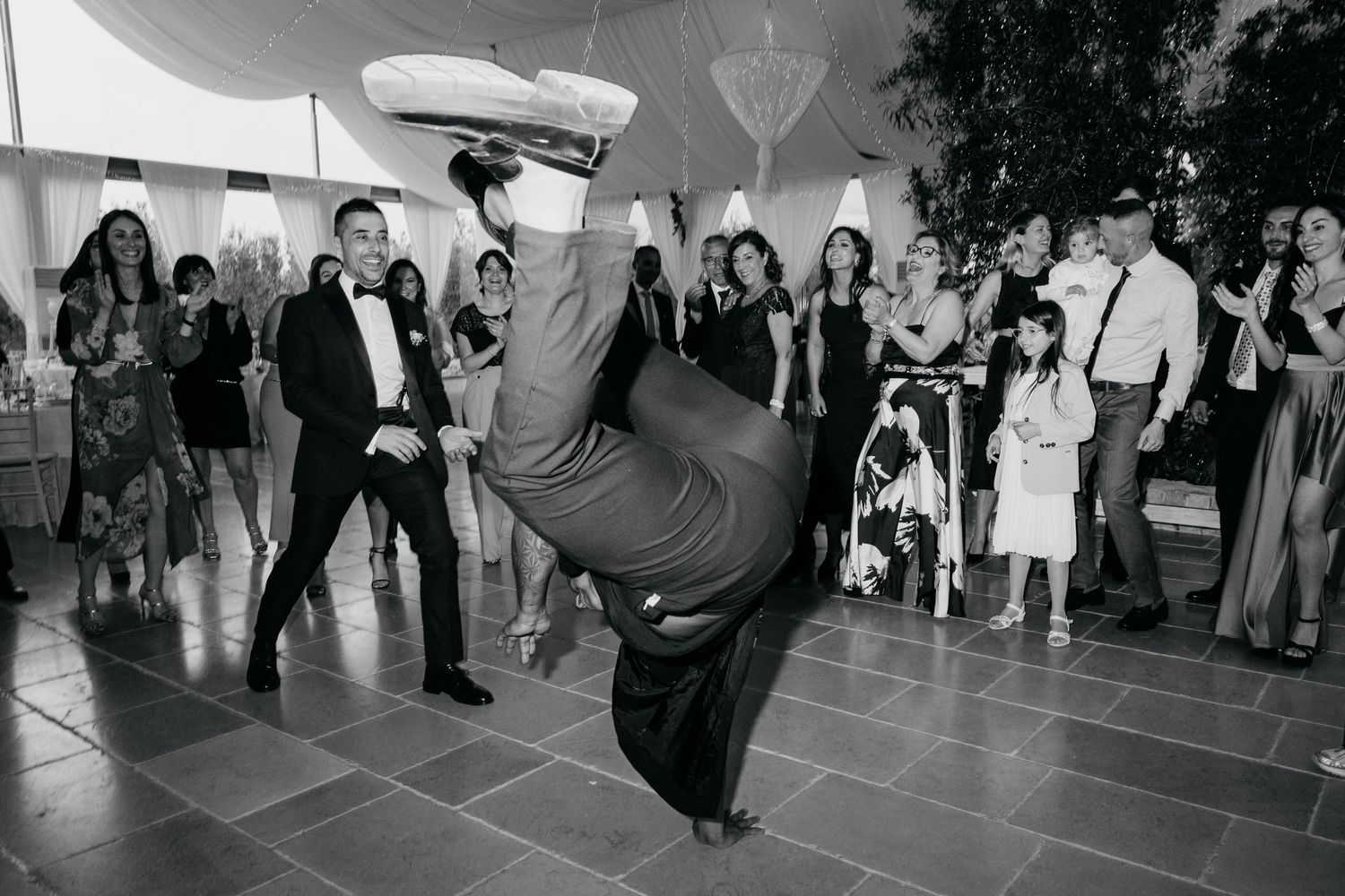 Person performing energetic dance move at formal event under tent.
