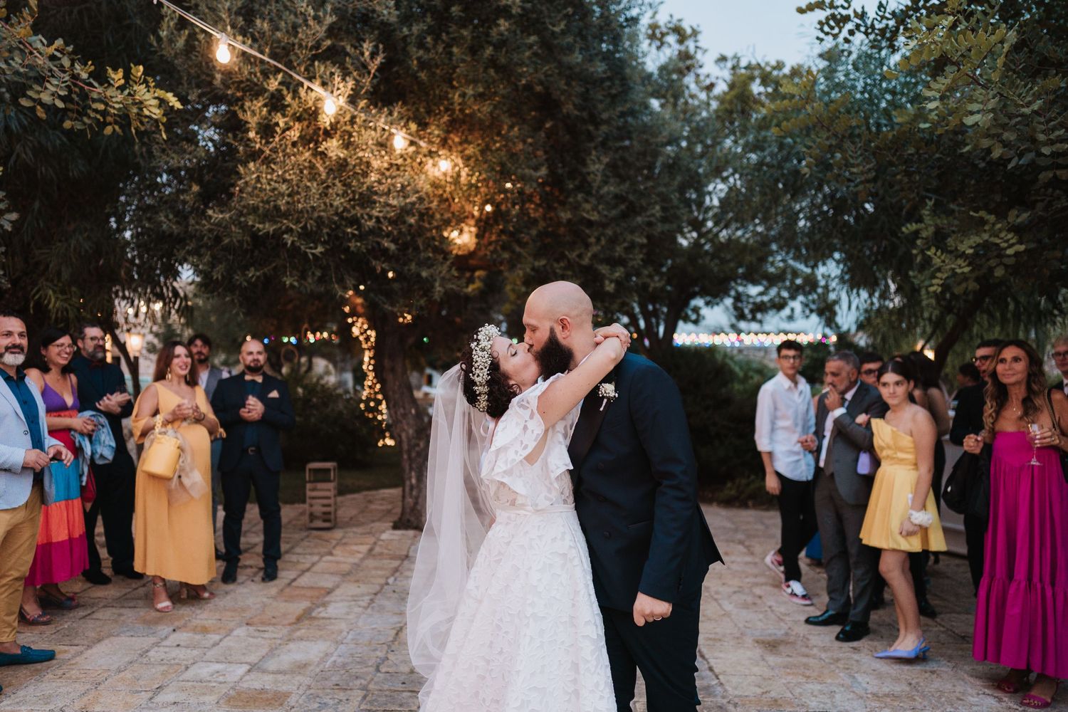 A romantic outdoor wedding reception under string lights with guests gathered around the dancing couple.