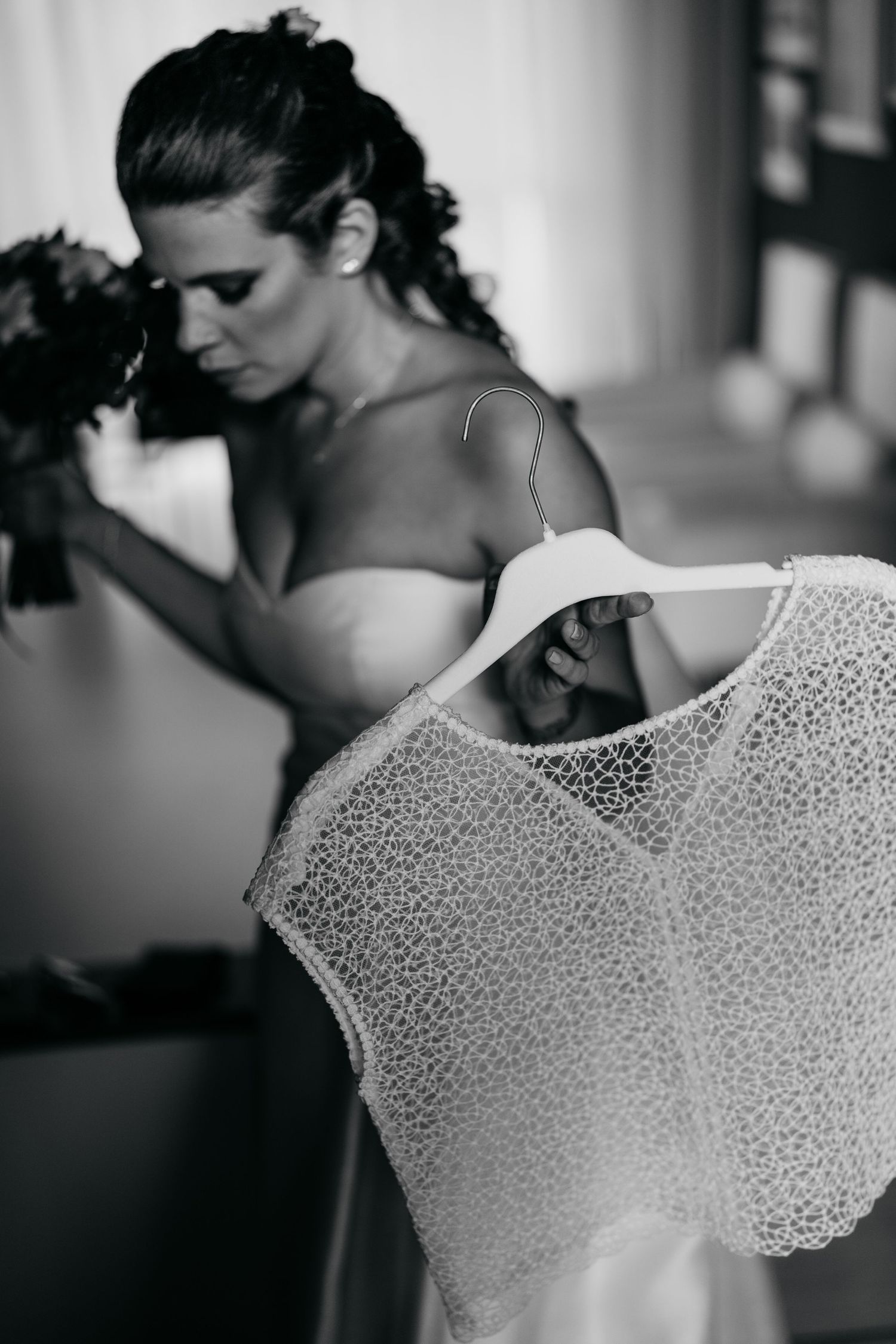 A close-up detail shot of a delicate white lace dress hanging in soft natural light.