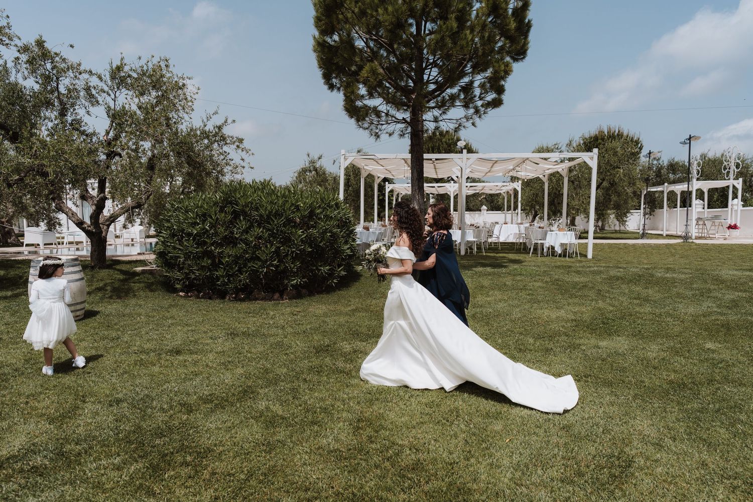 Wedding celebration in sunny garden with white pergola and trees.