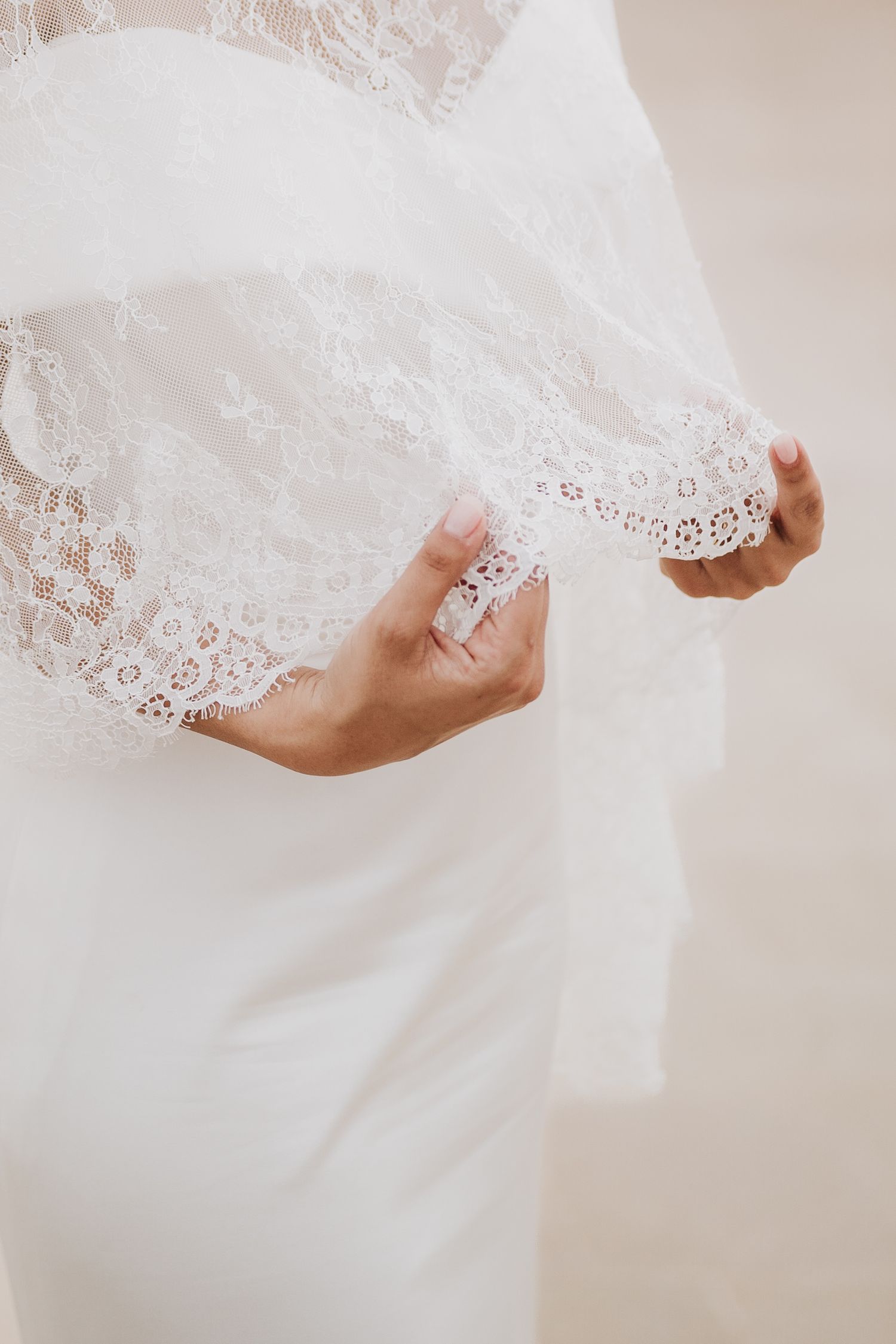Hands gently holding delicate lace detail on a white wedding gown.