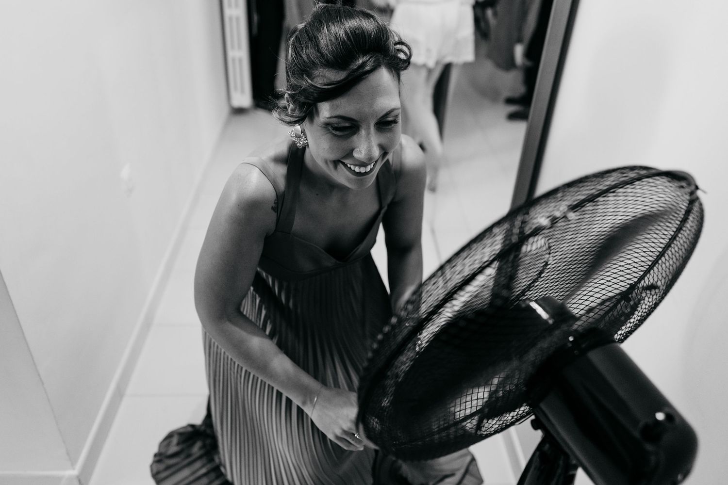 Black and white photo of someone in formal dress cooling off with an electric fan.