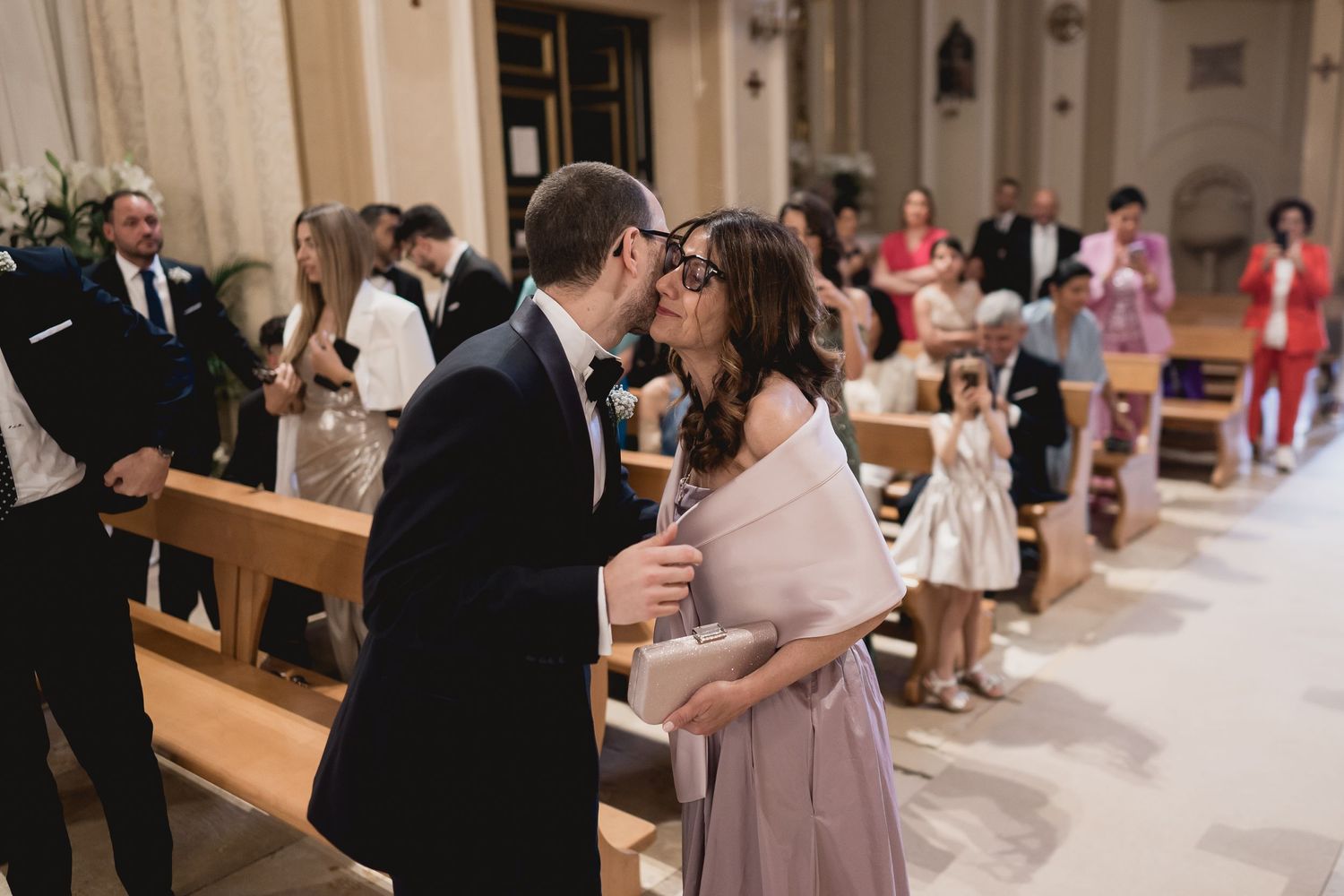 Wedding guests mingling in traditional church with wooden pews.