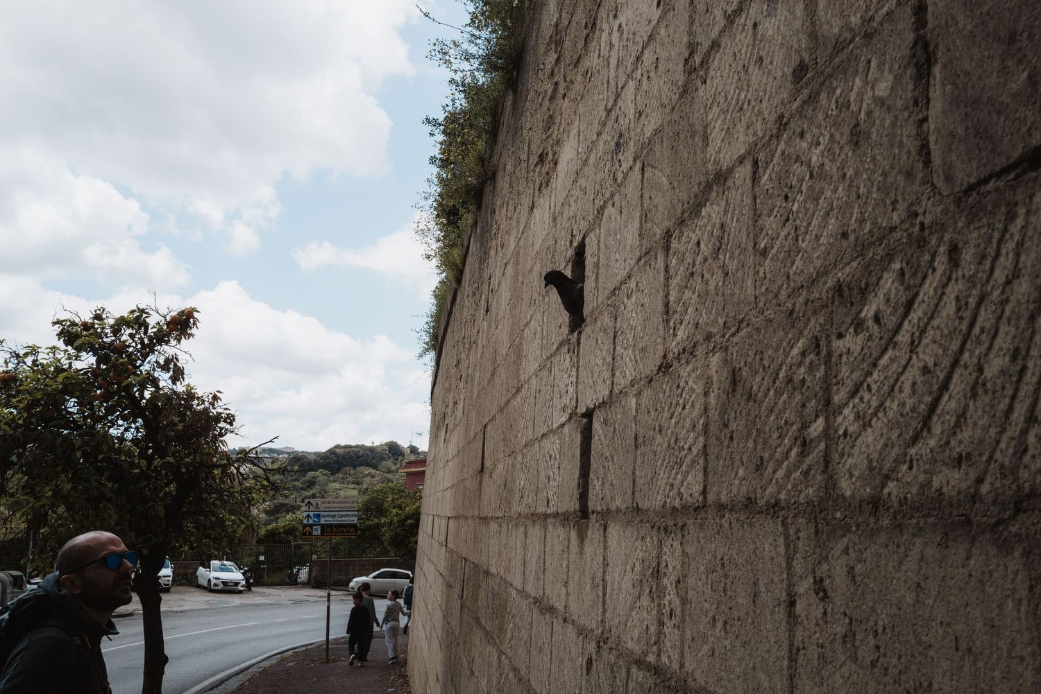 Stone city wall with small window openings under a cloudy sky.