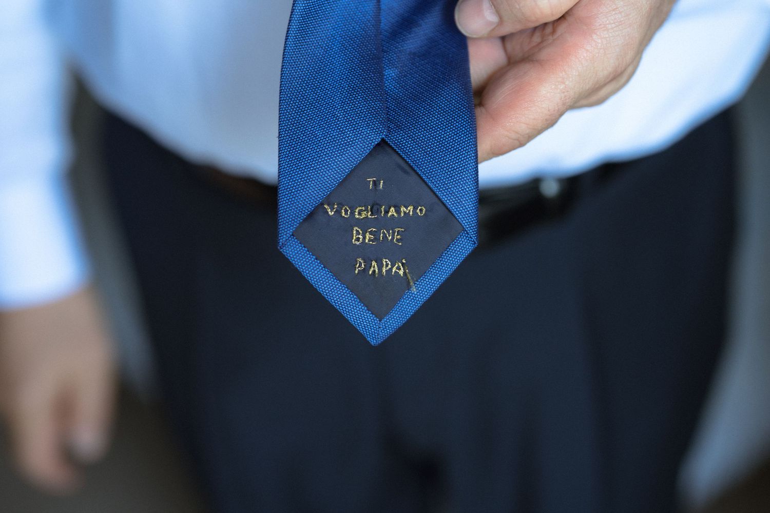 A close-up view of a blue diamond-shaped metal pin with text being attached to formal attire.
