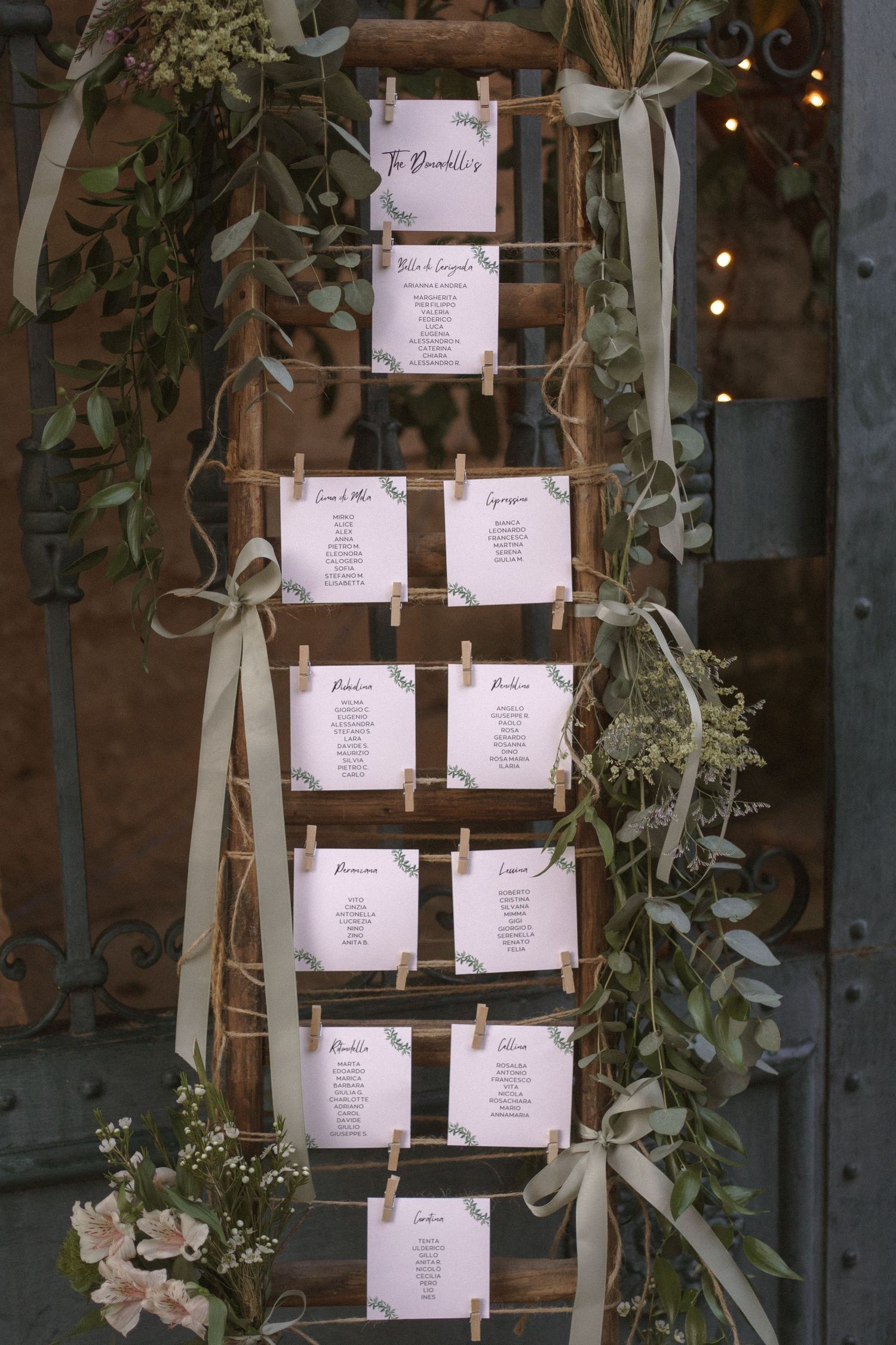 Elegant wedding seating chart display with white cards arranged on wooden ladder with greenery.